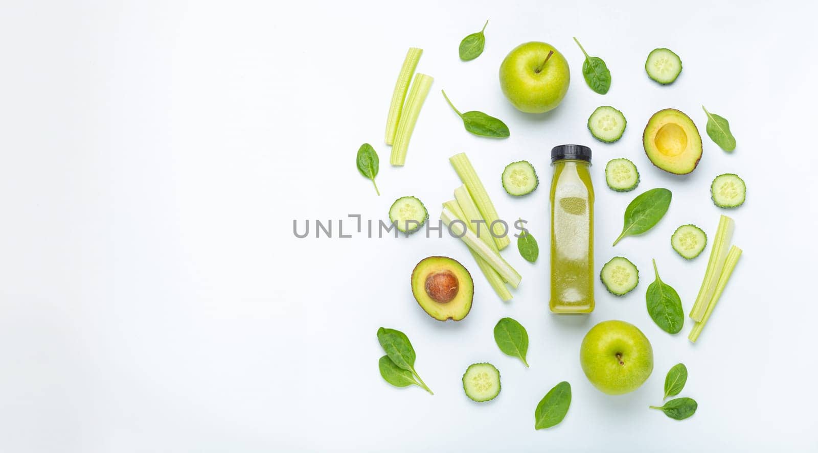 Bottle of green smoothie surrounded by green fruit and vegetables: apples, avocado, spinach, celery, cucumber on white simple background top view. Diet, healthy nutrition, detox concept, copy space by its_al_dente