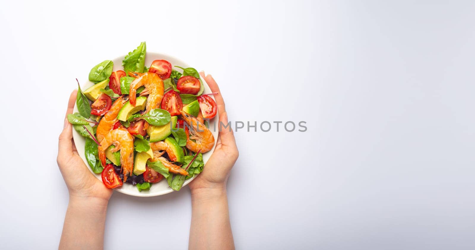 Female hands holding salad with grilled shrimps, avocado, vegetables, green leaves on white plate isolated on white background top view. Clean eating, nutrition and dieting concept, copy space. by its_al_dente