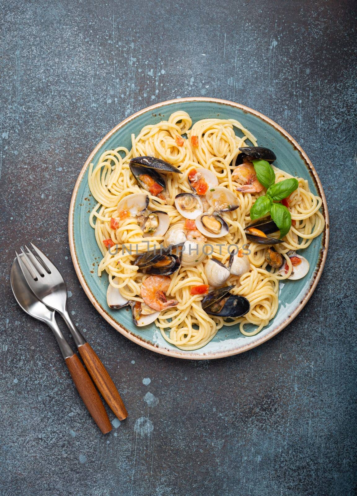 Italian seafood pasta spaghetti with mussels, shrimps, clams in tomato sauce with green basil on plate on rustic blue concrete background overhead. Mediterranean cuisine