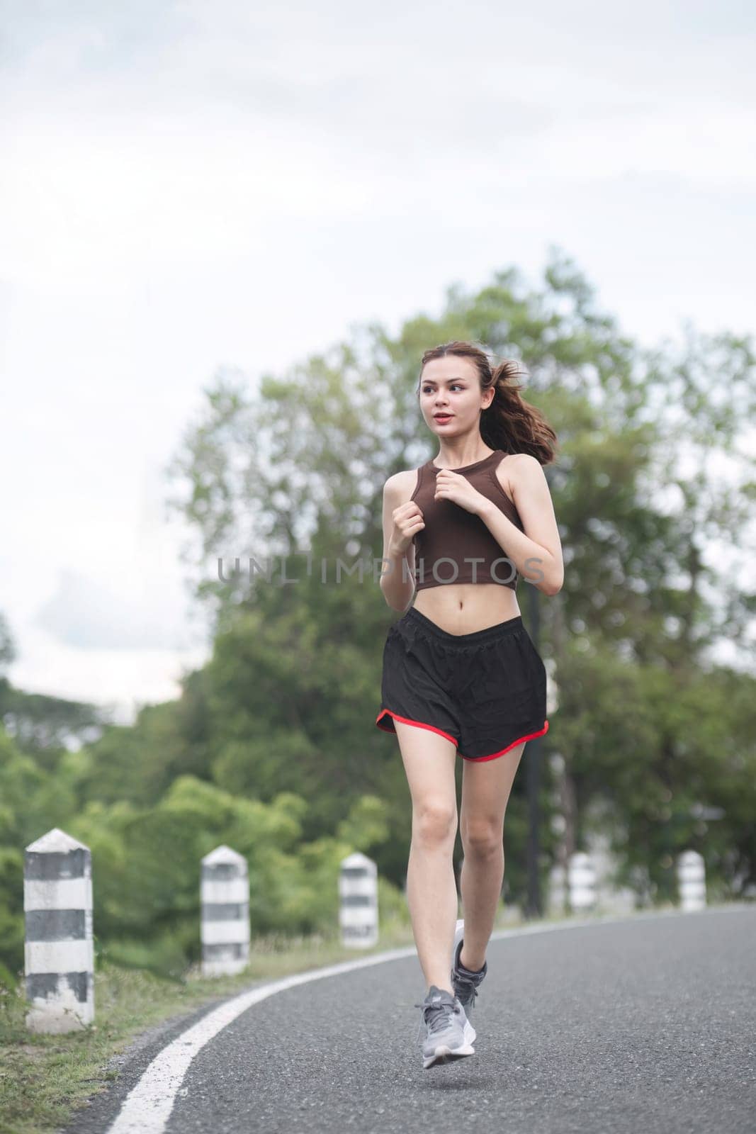 Young sporty woman jogging in the green park in the evening by wichayada