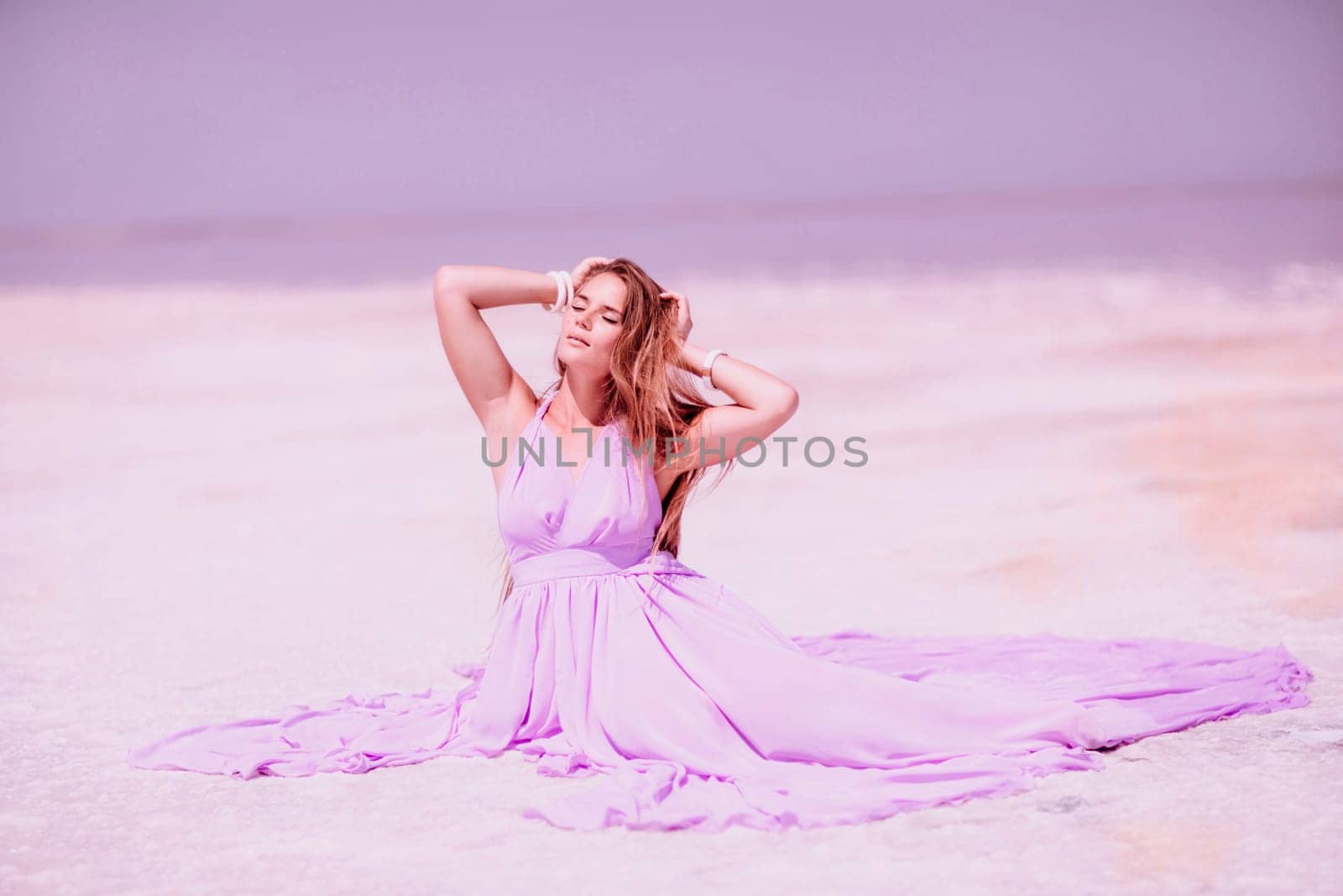 Pink lake woman. A woman in a pink dress sits on the salty shore of a pink lake and poses for a souvenir photo, creating lasting memories