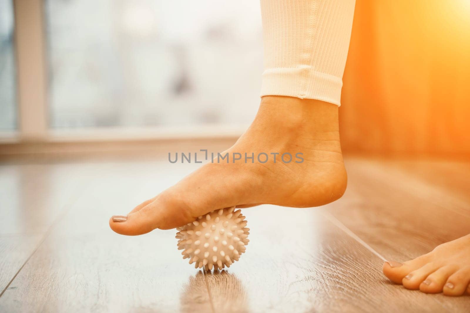 Athletic slim caucasian woman doing thigh self-massage with a massage ball indoors. Self-isolating massage by Matiunina