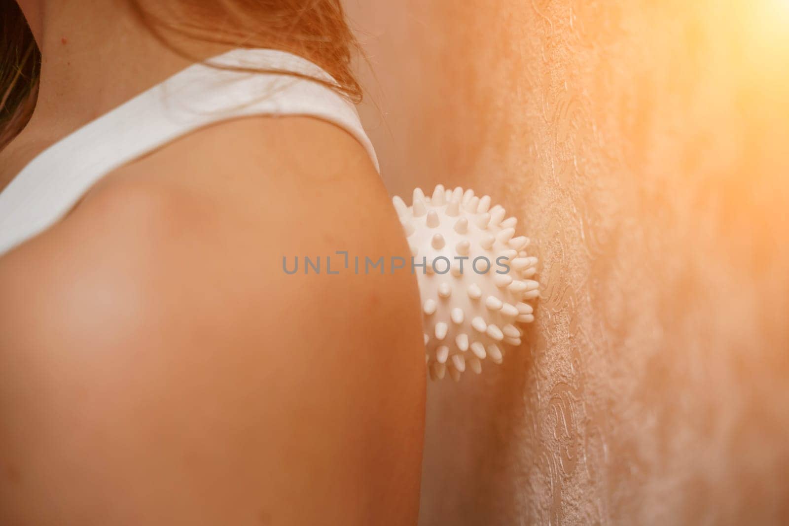 Athletic slim caucasian woman doing thigh self-massage with a massage ball indoors. Self-isolating massage.