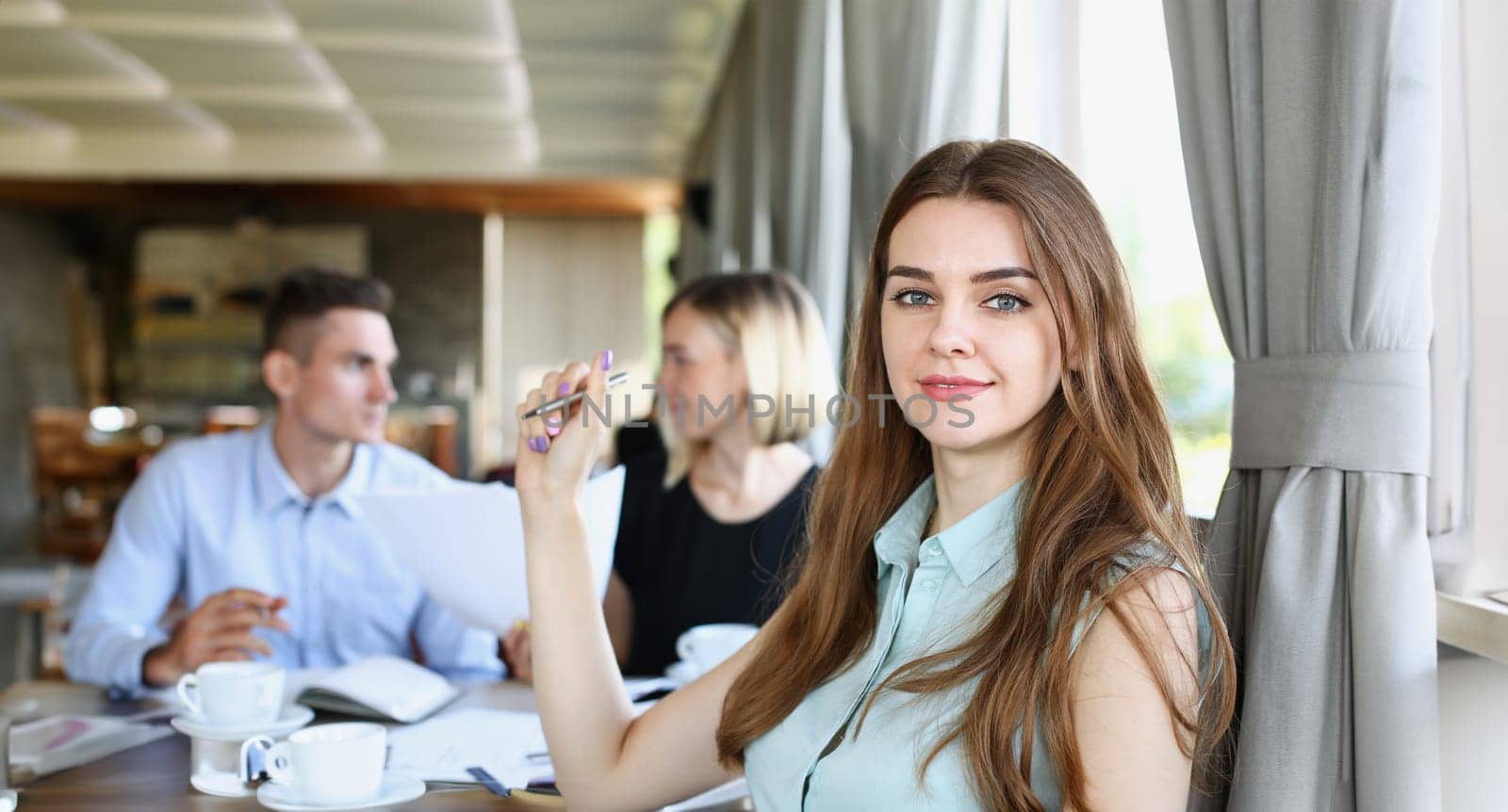 Beautiful smiling cheerful girl at cafe look in camera with colleagues group in background. White collar worker at workspace job offer modern lifestyle client visit profession train concept