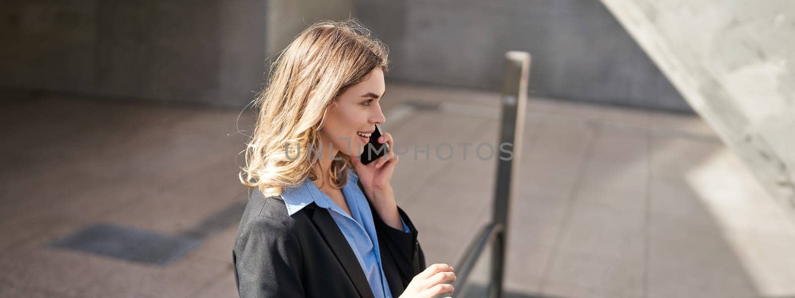 Corporate woman talking on mobile phone, making a call while in city, standing outdoors on escalator.