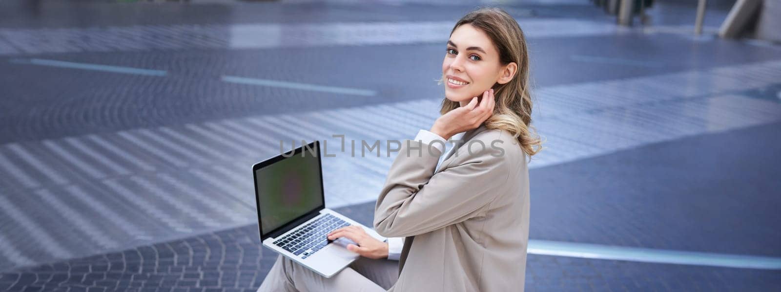 Young digital nomad, businesswoman sitting with laptop in city centre. Office worker using computer outdoors.