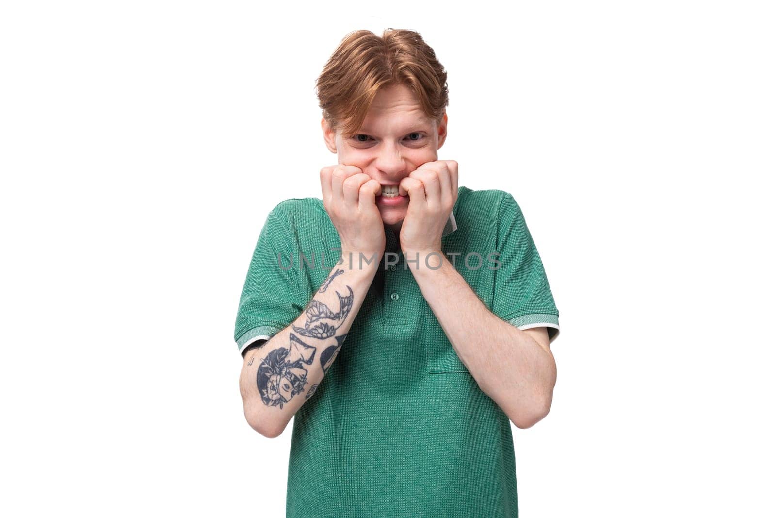 young stylish european guy with red hair with a tattoo on his forearm wears a green t-shirt has doubts.