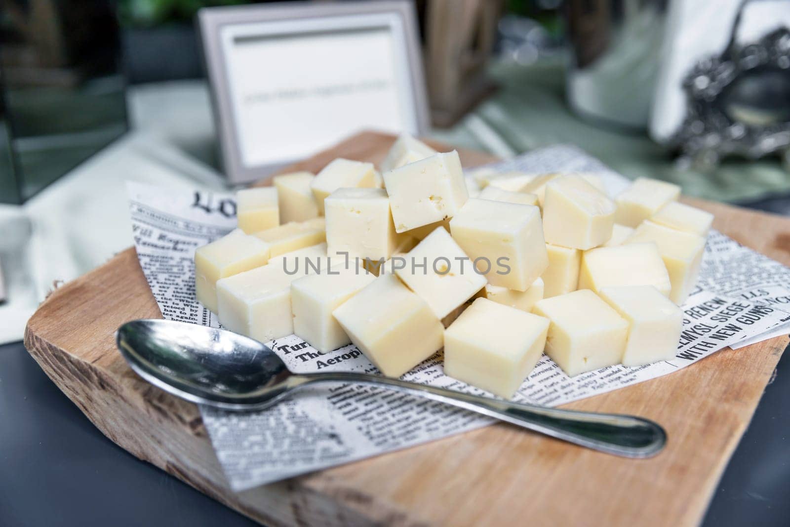 Pieces and cubes of cheese on wood cutting board, with spoon. Party. Events.