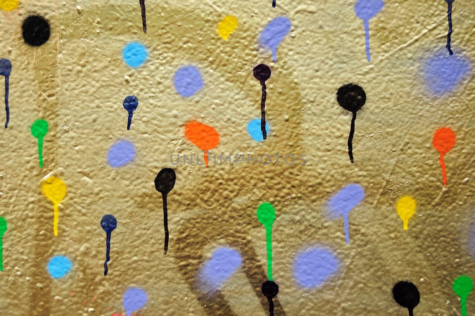 Golden painted wall covered with dots of dripping spray paint.