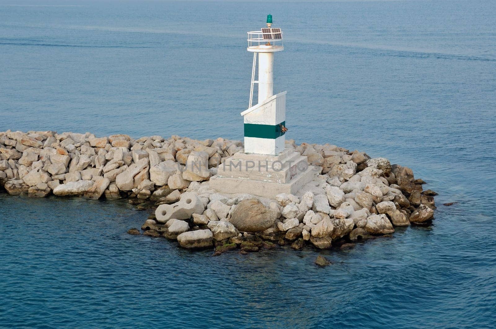Modern automated lighthouse by the sea and rock jetty at port entrance.