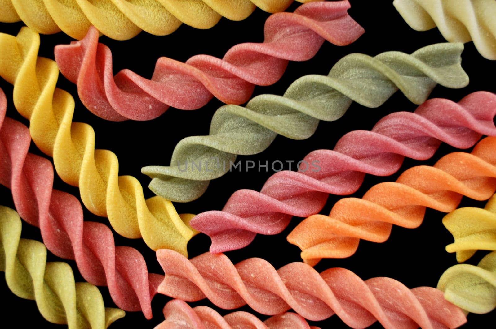 Multi colored fusilli italian pasta on black background. Creative food.
