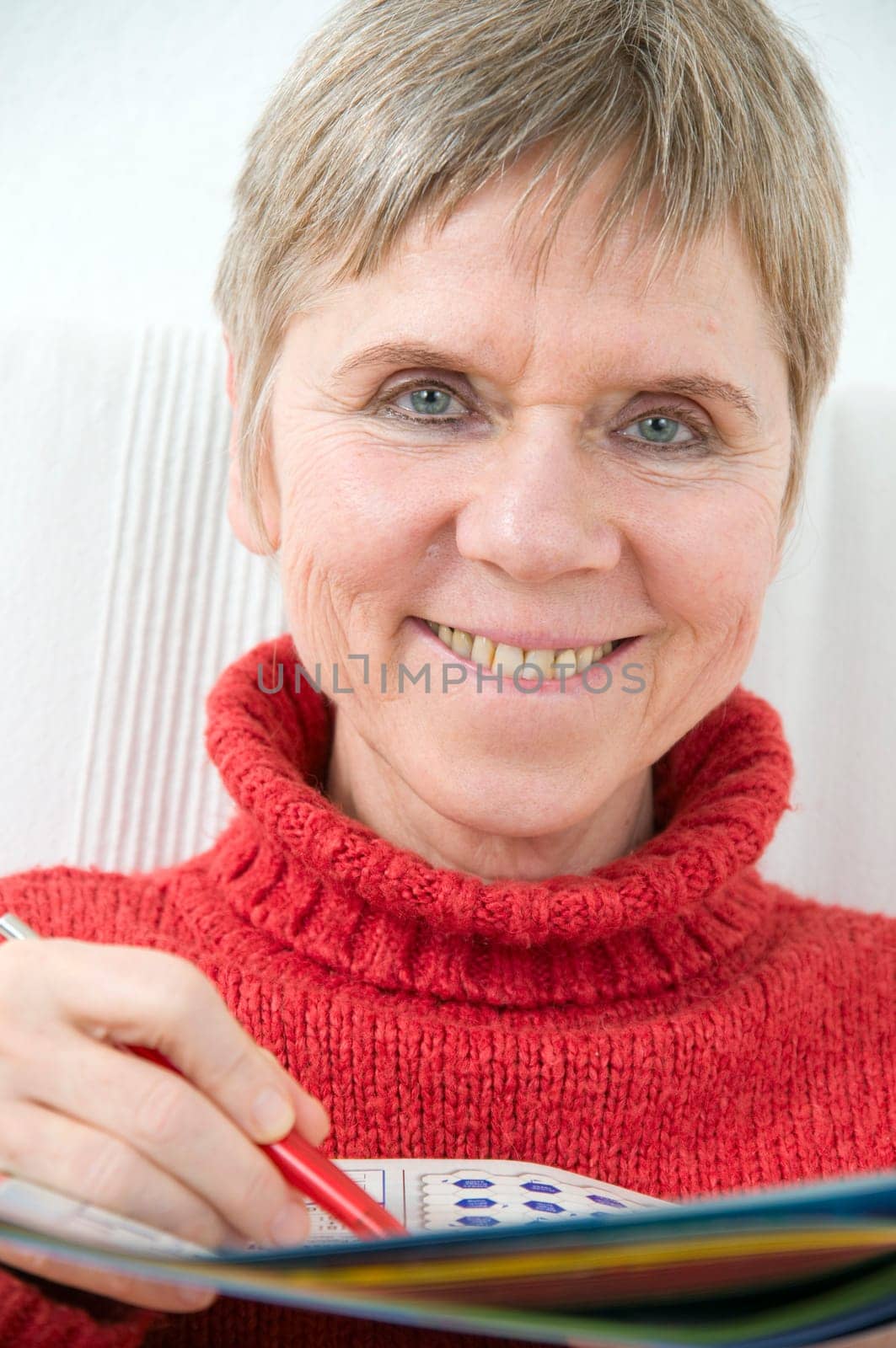 Head and shoulders portrait of a mature woman in a red sweater,puzzle book and pen
