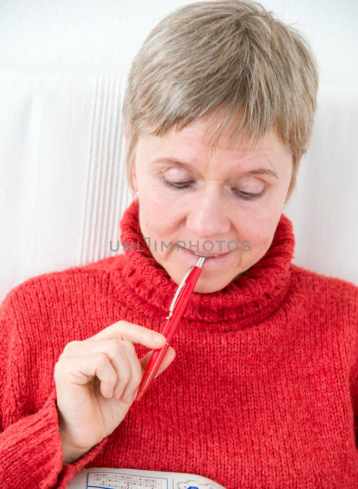 Head and shoulders portrait of a mature woman in a red sweater,puzzle book and pen
