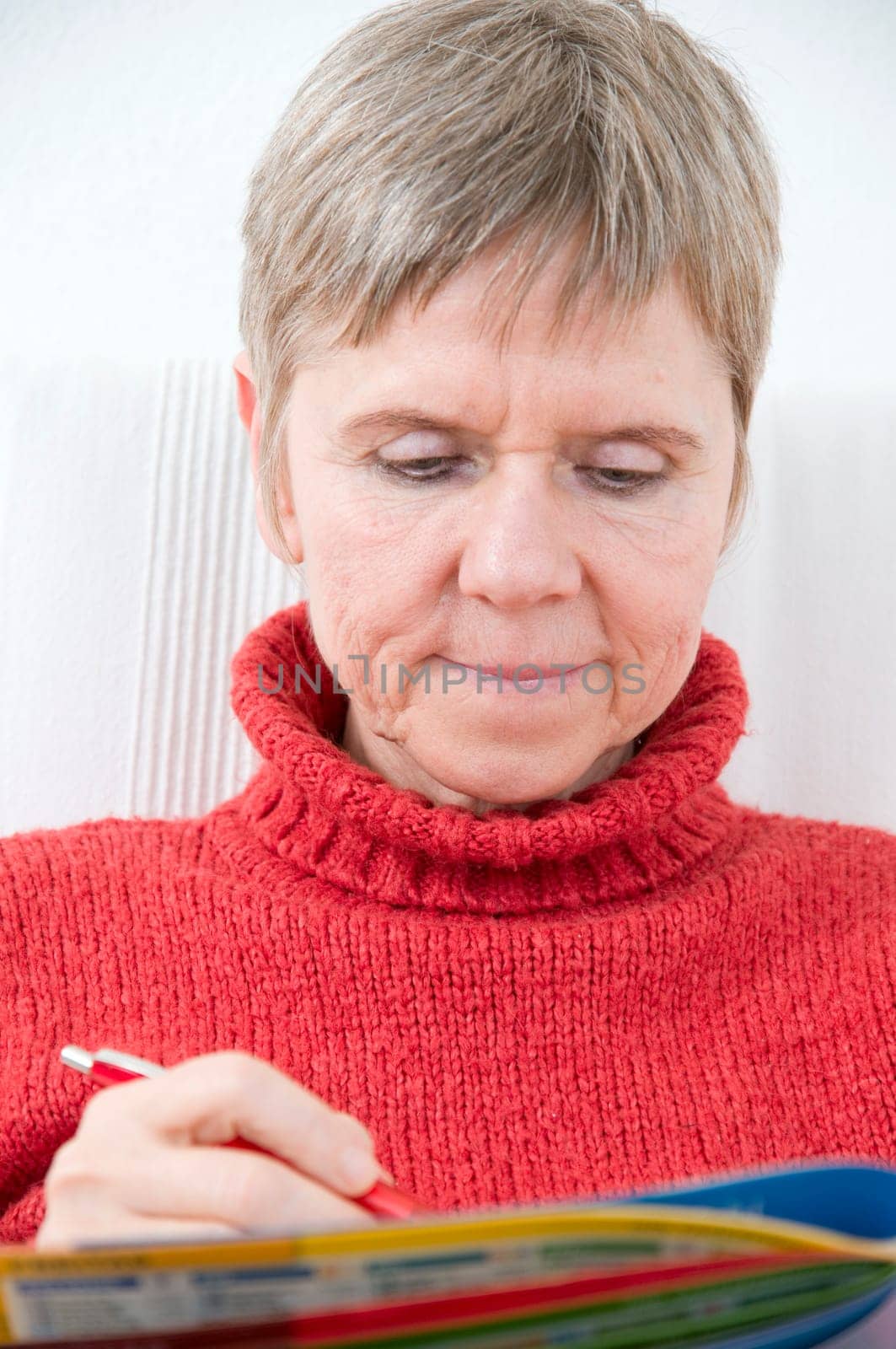 Head and shoulders portrait of a mature woman in a red sweater,puzzle book and pen