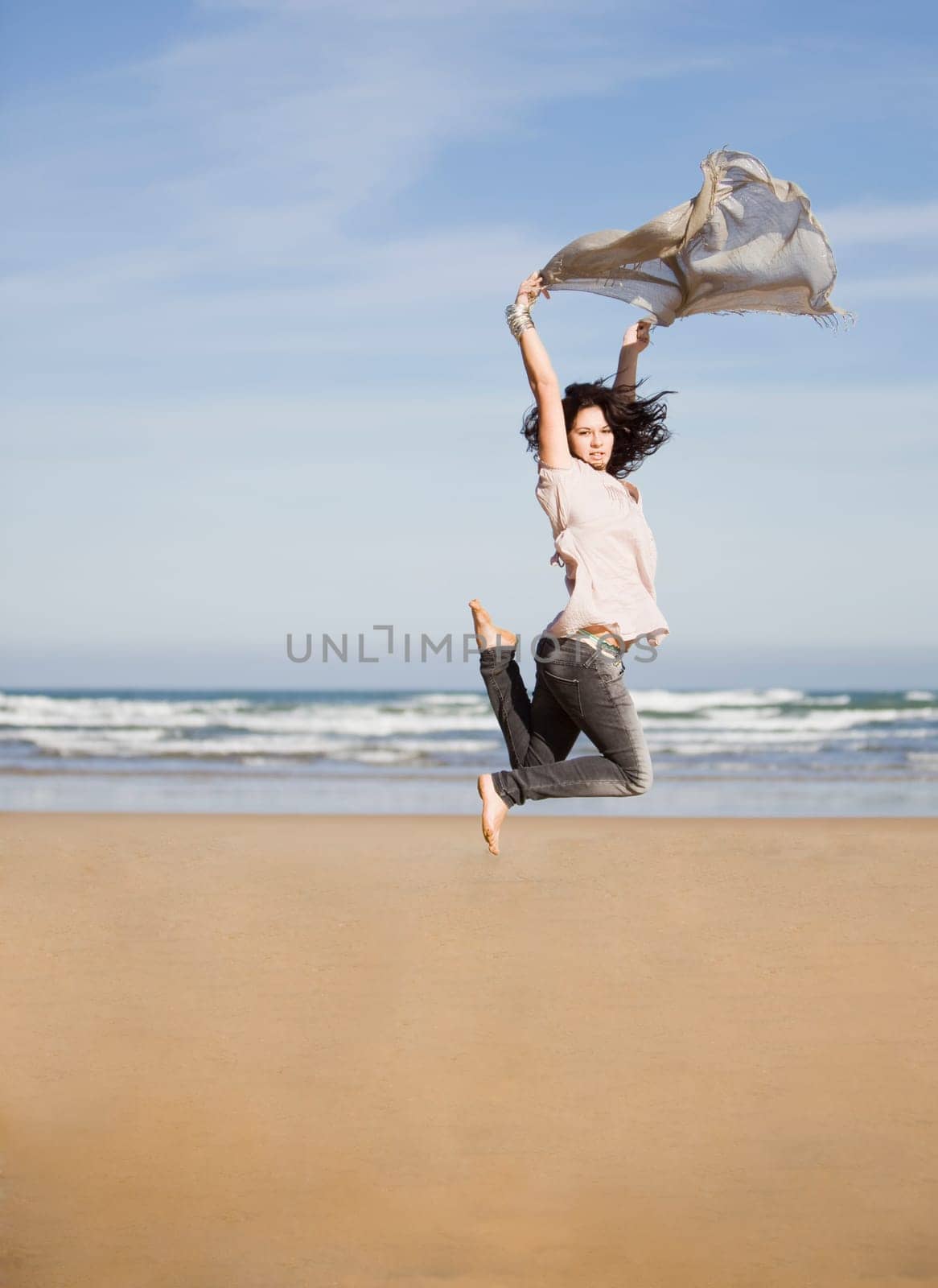 beautiful happy young girl running and jumping over a windy beach with a blowing scarf