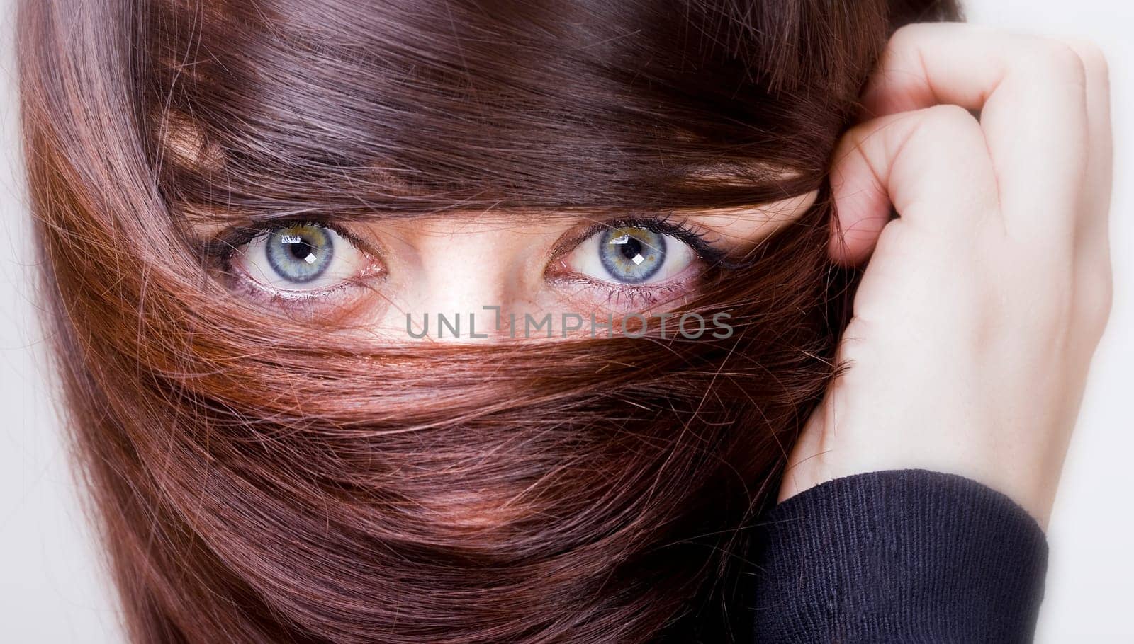 extrange look of a young woman with blue eyes with her hair around the eyes