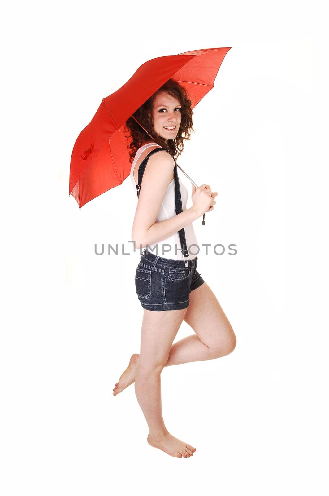 A young pretty woman in jeans shorts with suspender and a white t-shirt standing bare feet and holding an umbrella over her shoulder, over white.