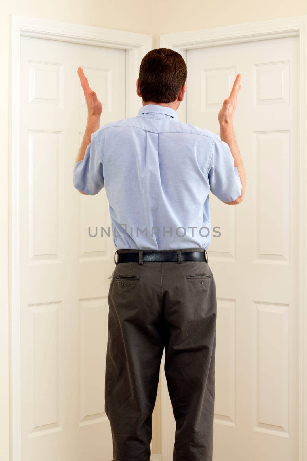 Man between two doors with hands in the air not sure which to choose.