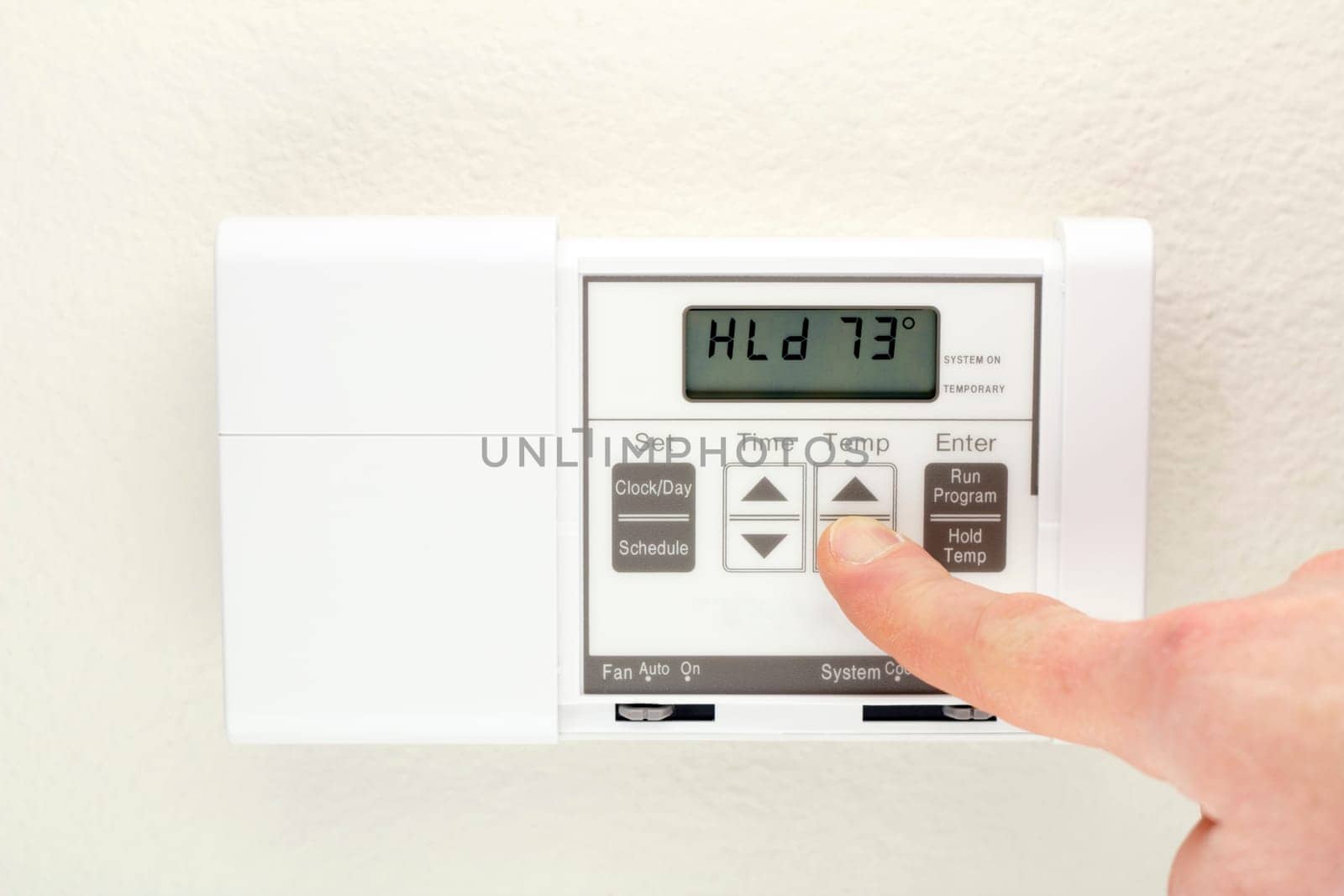 Finger pushing control buttons on heating and cooling digital wall panel display.