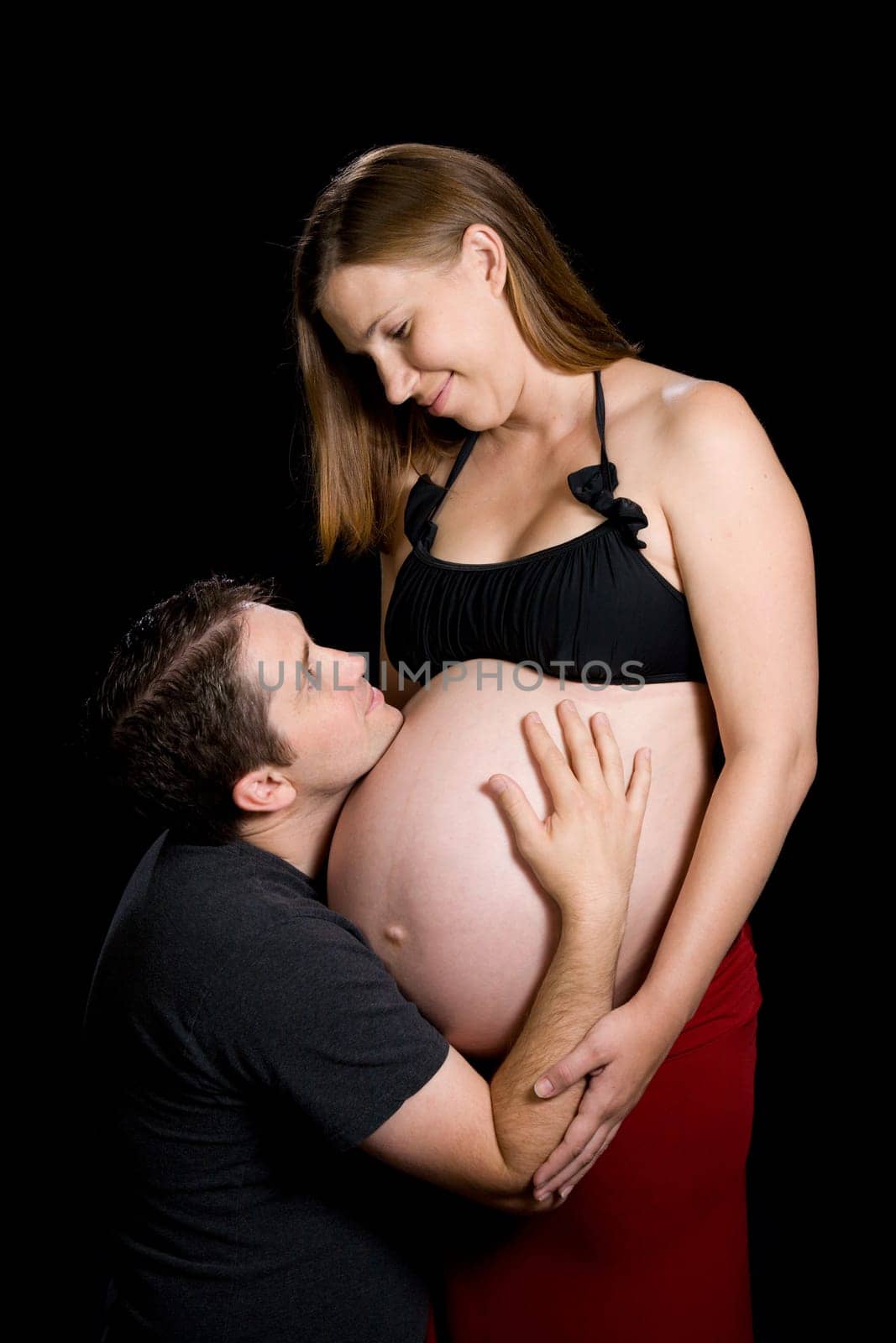 A man is embracing his pregnant wife&#039 s belly.