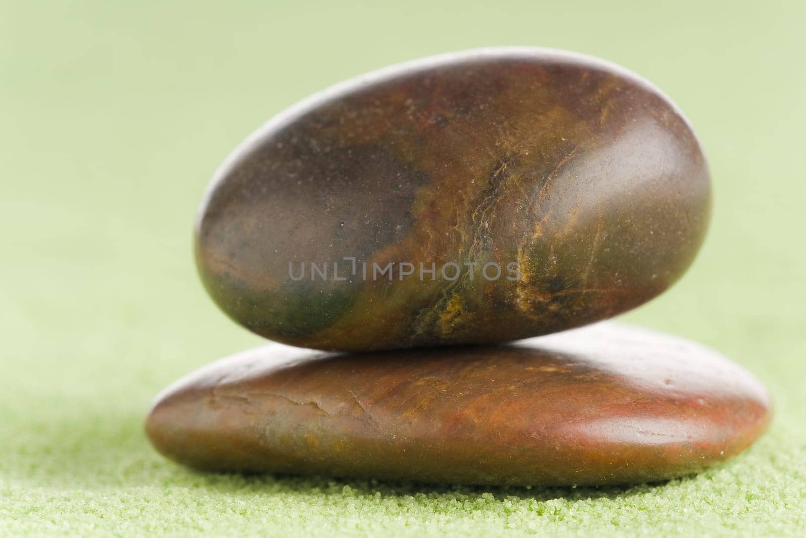 Brown flat and round stones in balance on green sand