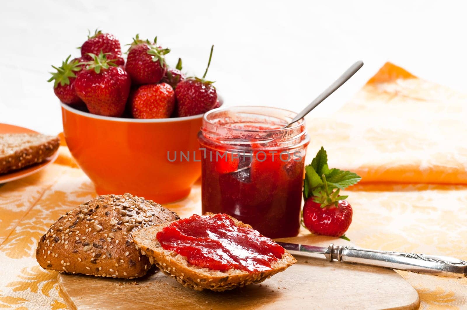 Breakfast table with strawberry jam,rolls,fresh strawberries on breakfast board