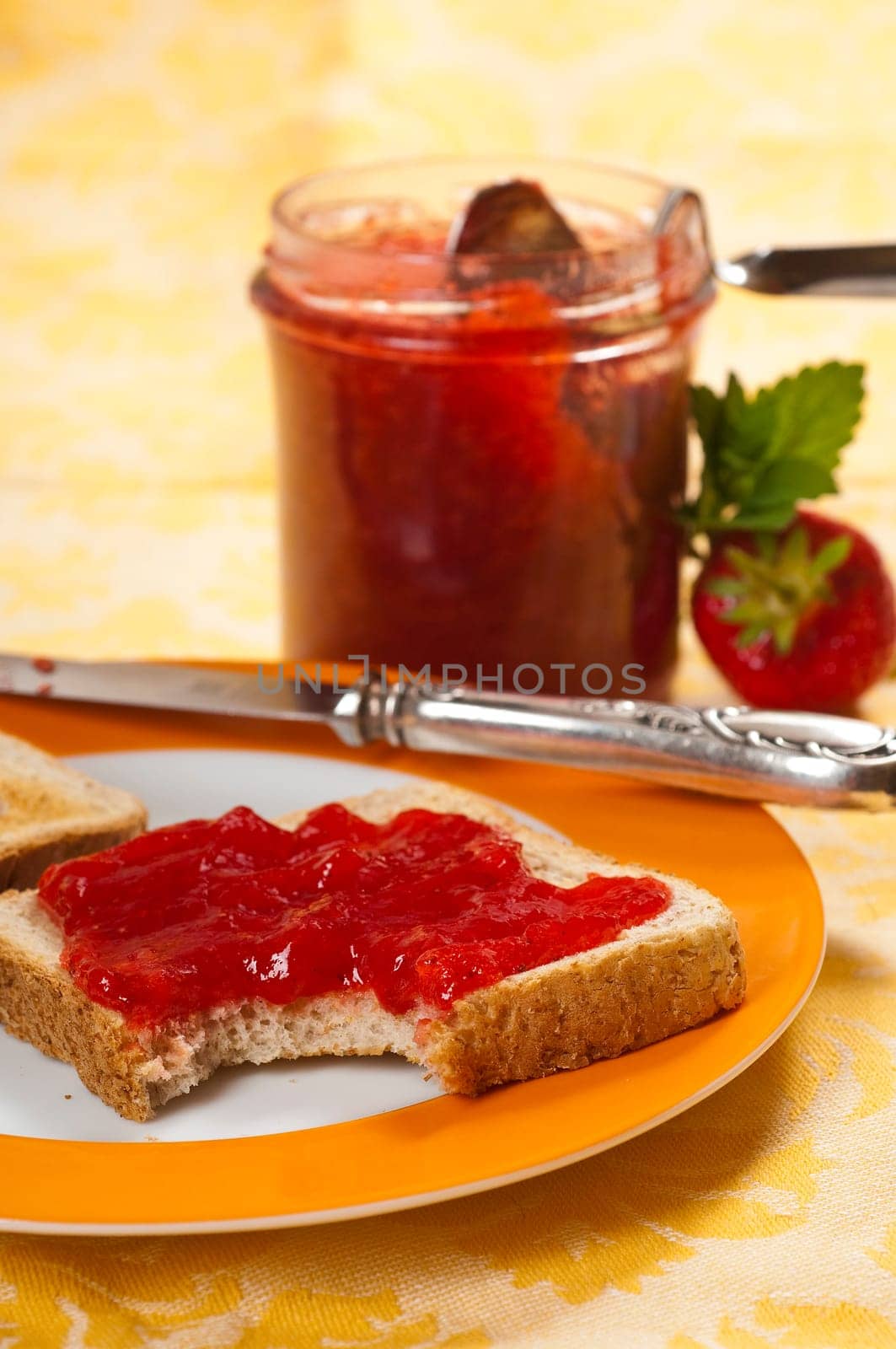 Breakfast table with strawberry jam,toast,fresh strawberries in bowl,porcelain plate