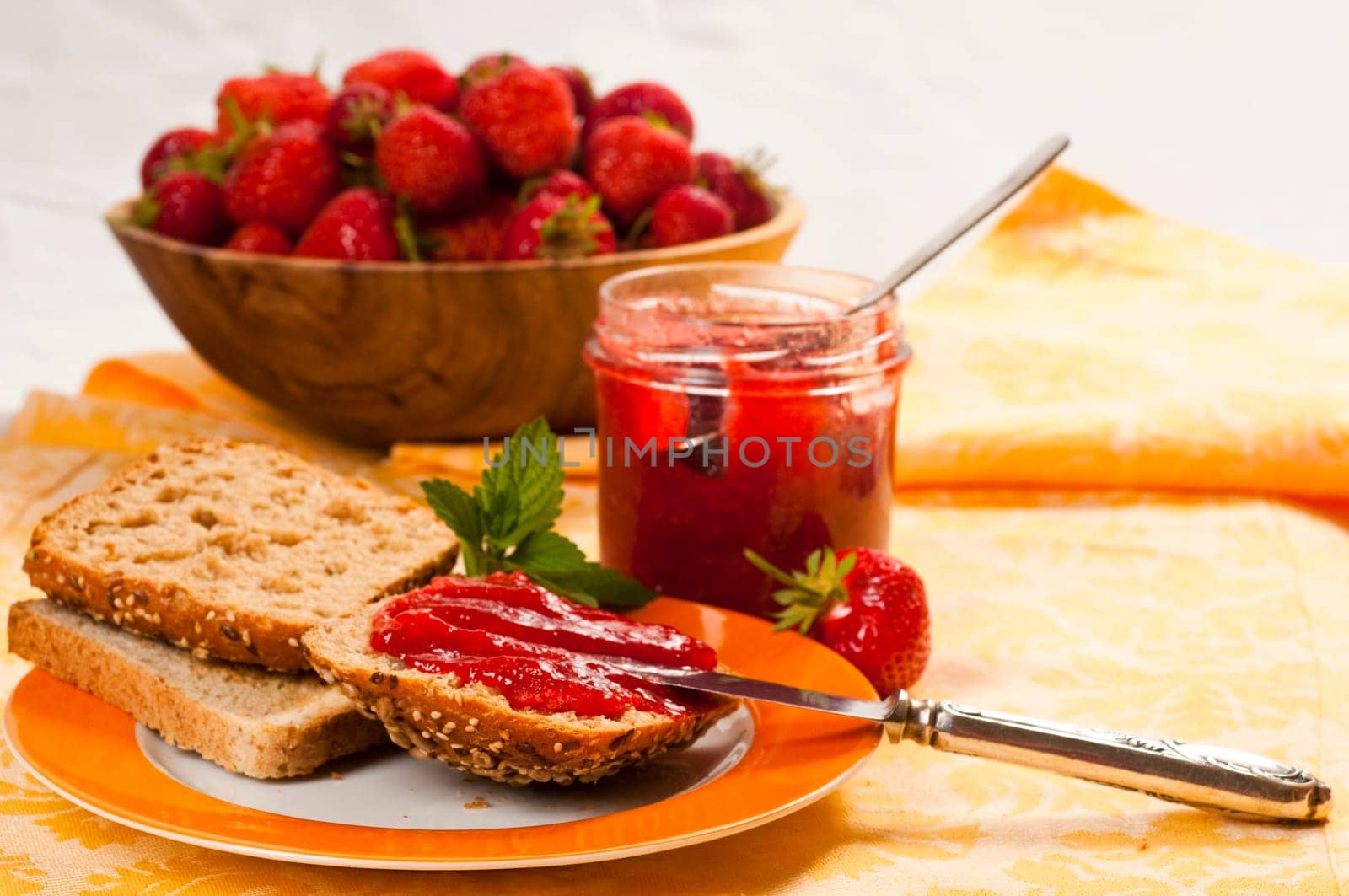 Breakfast table with strawberry jam,rolls,fresh strawberries,on an orange porcelain plate