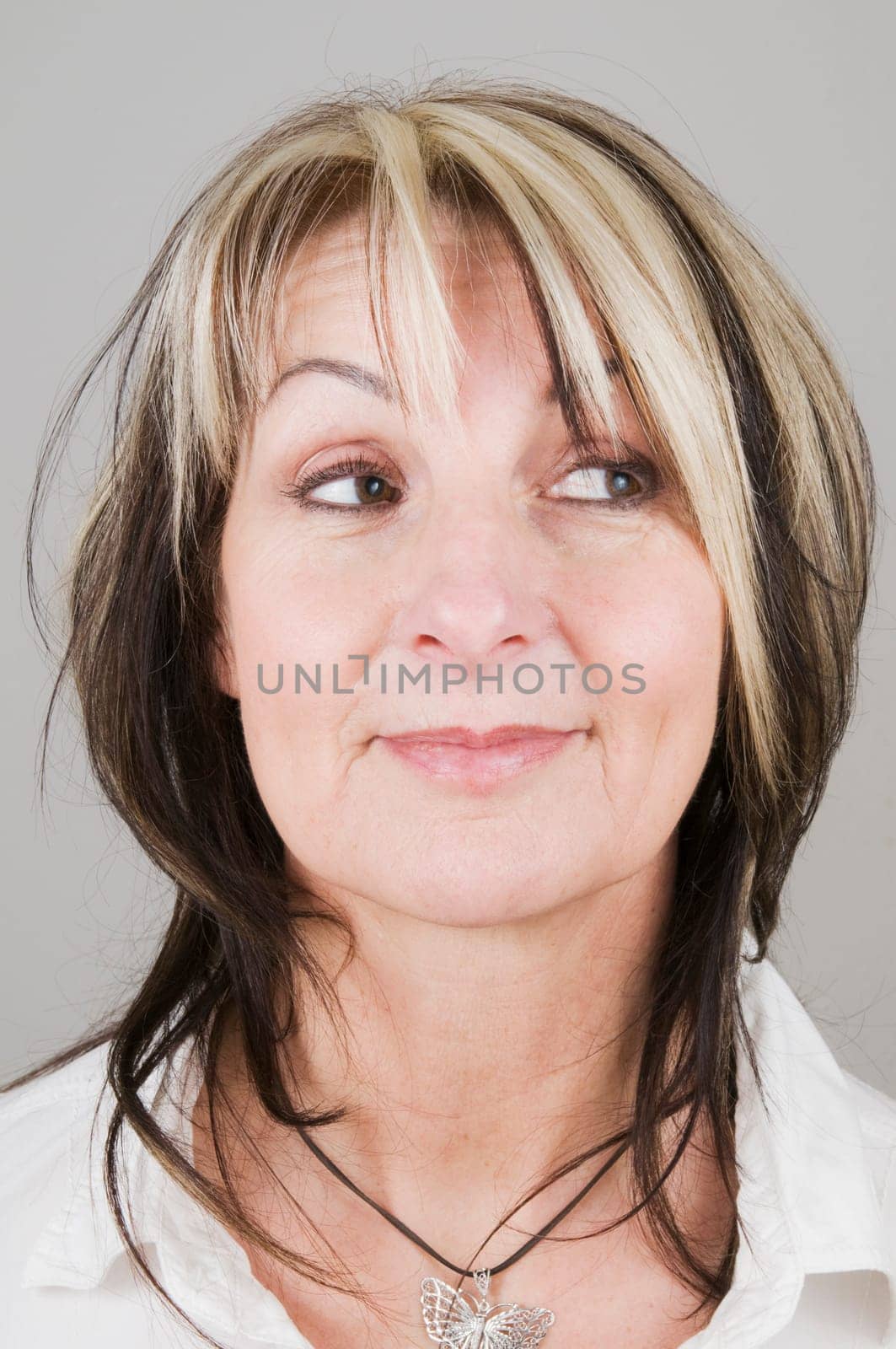 Head portrait of a mature blonde woman with dark streaks looking to the side with only her eyes