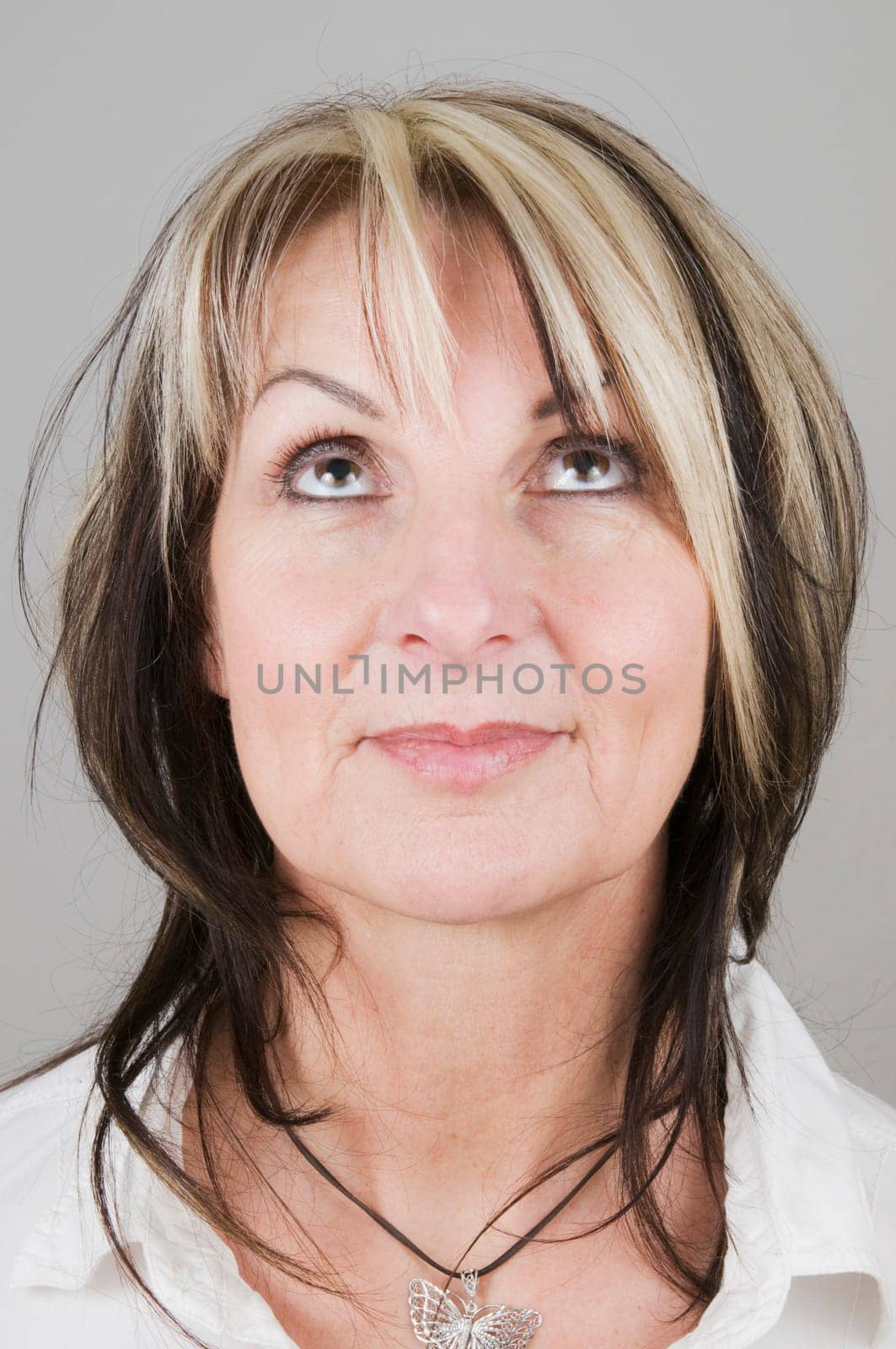 Head portrait of a mature blonde woman with dark streaks looking up with only her eyes