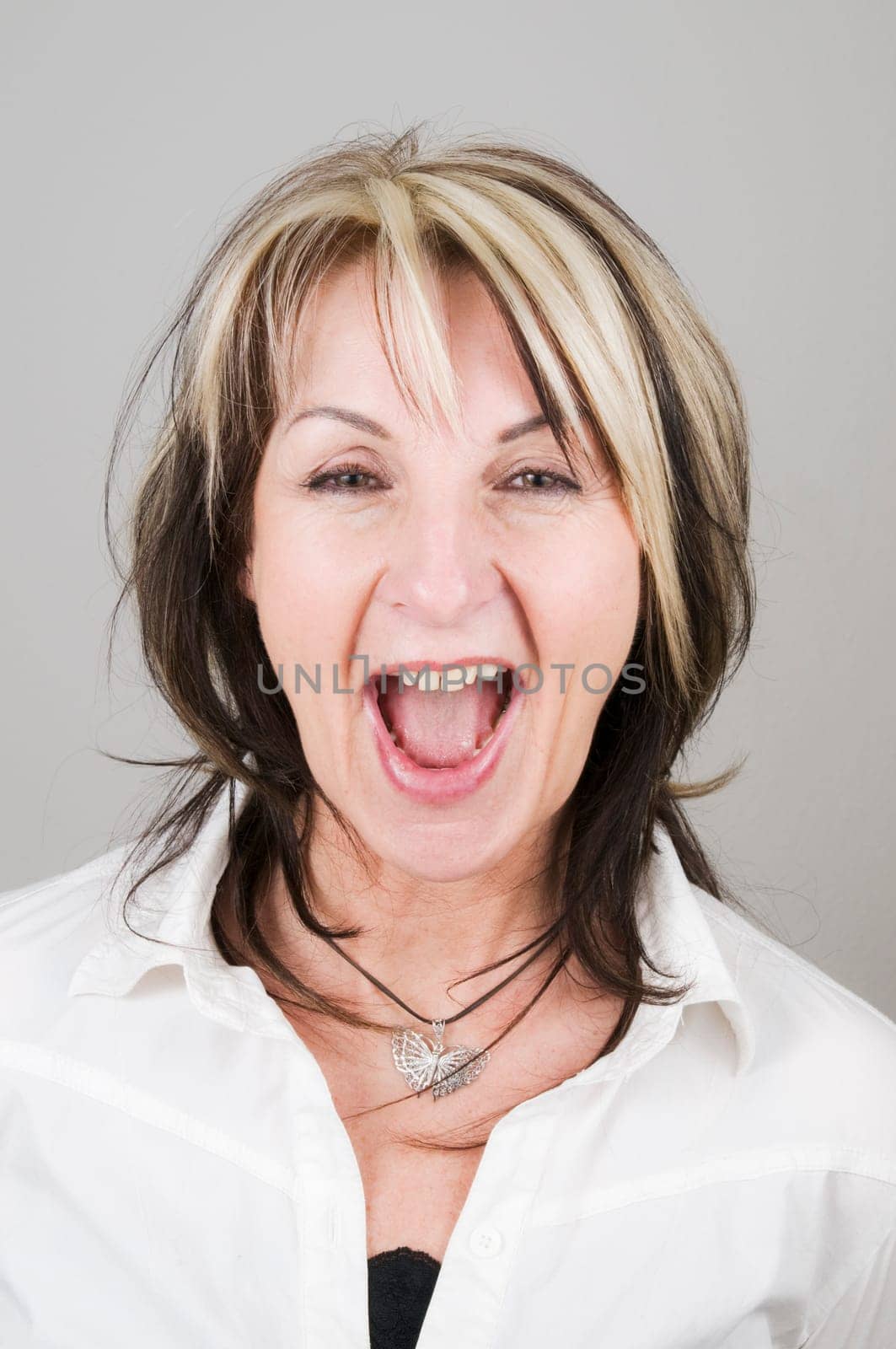 Head portrait of a mature blonde woman with dark streaks looking at the camera with her mouth open and head-on