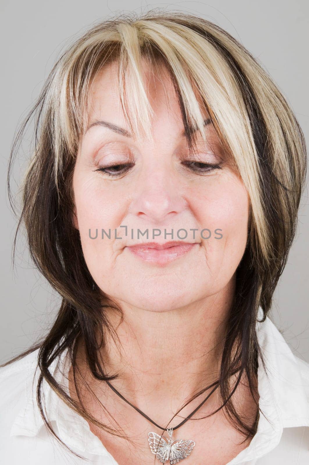 Head portrait of a mature blonde woman with dark streaks looking down only with her eyes