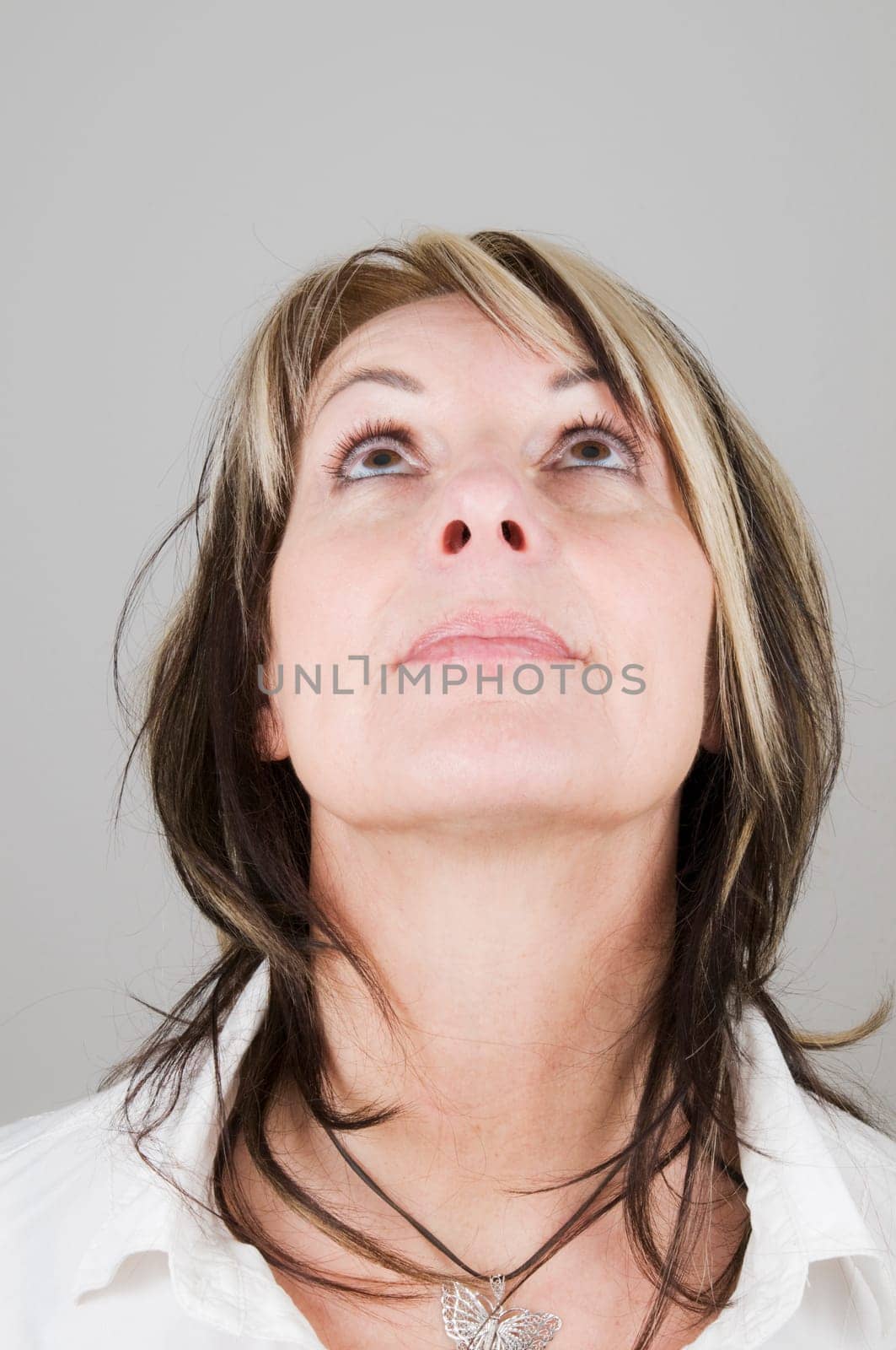 Head portrait of a mature blonde woman with dark streaks looking up with only her eyes