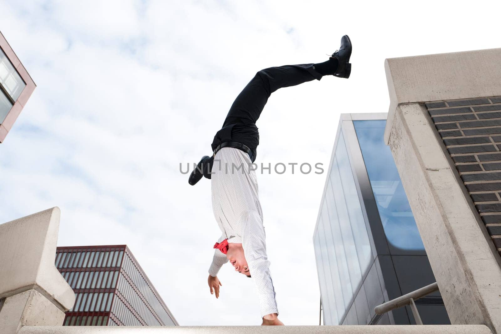 Young businessman in handstand in front of sky and house front
