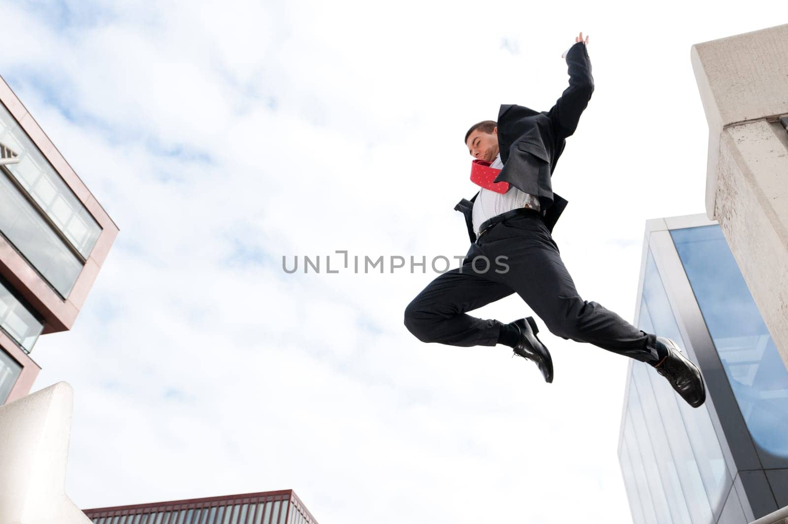 Young businessman jumping in front of sky and house front
