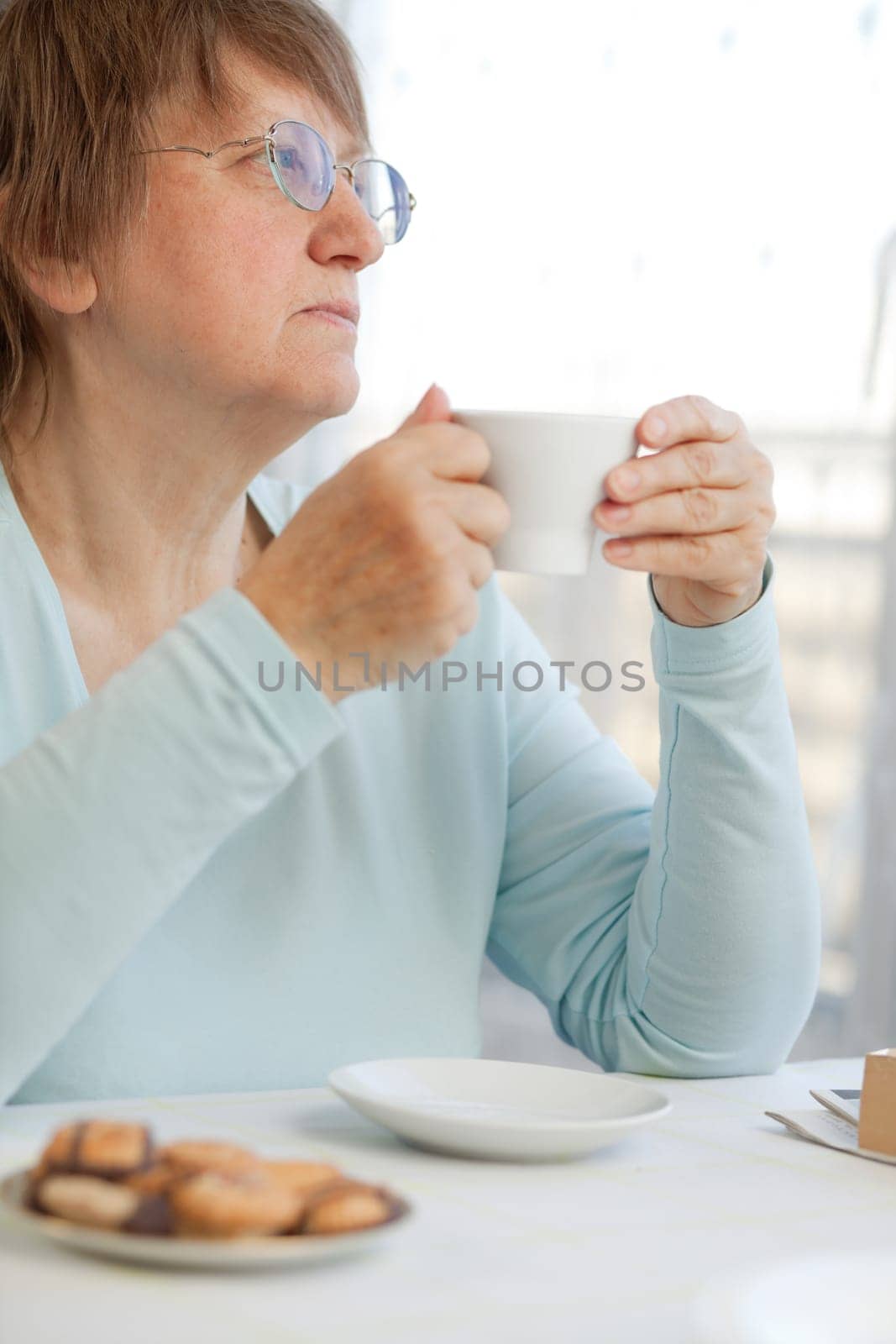 Elderly woman enjoying a cup of coffee with cookies at home