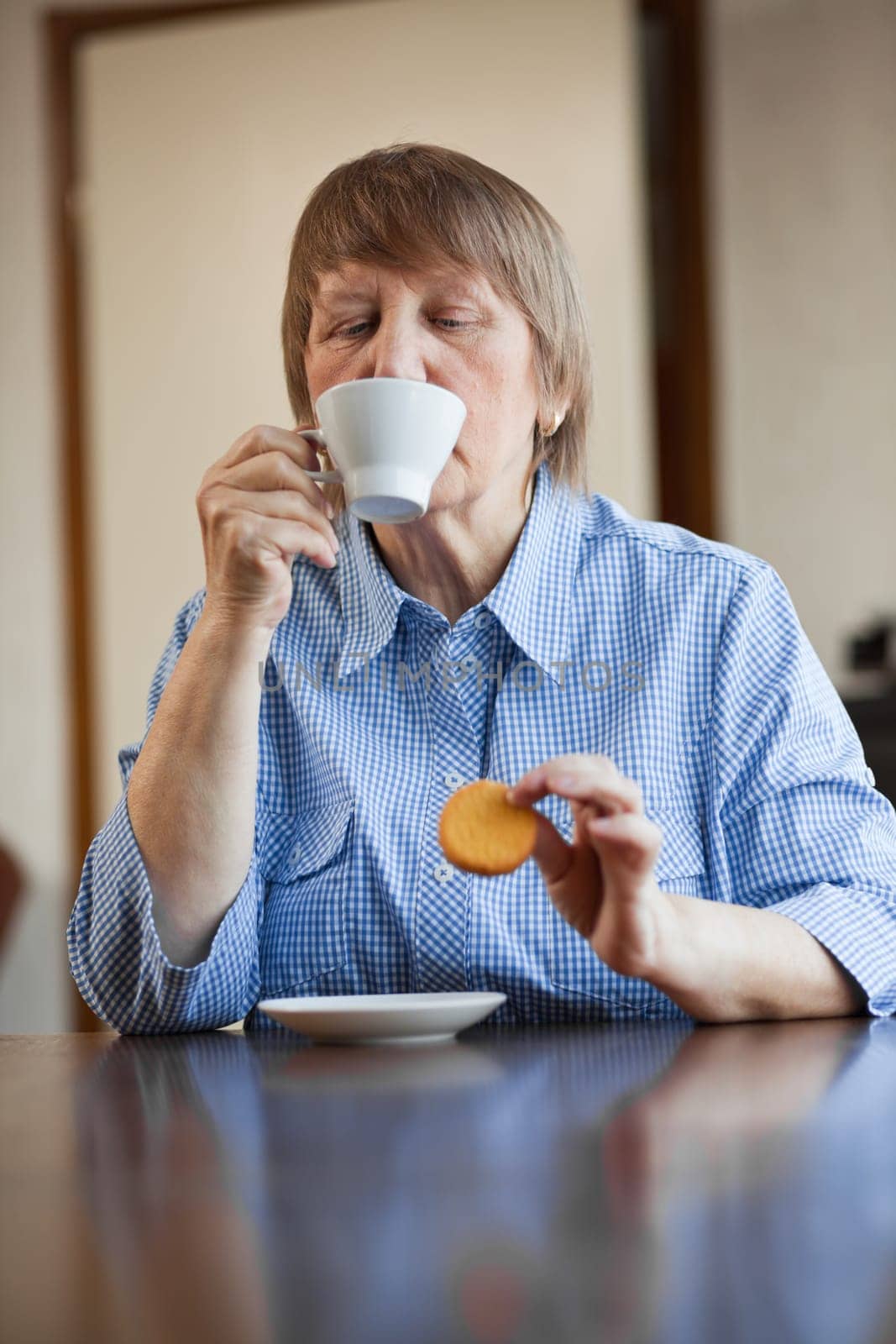 Elderly woman enjoying a cup of coffee and cookie at home