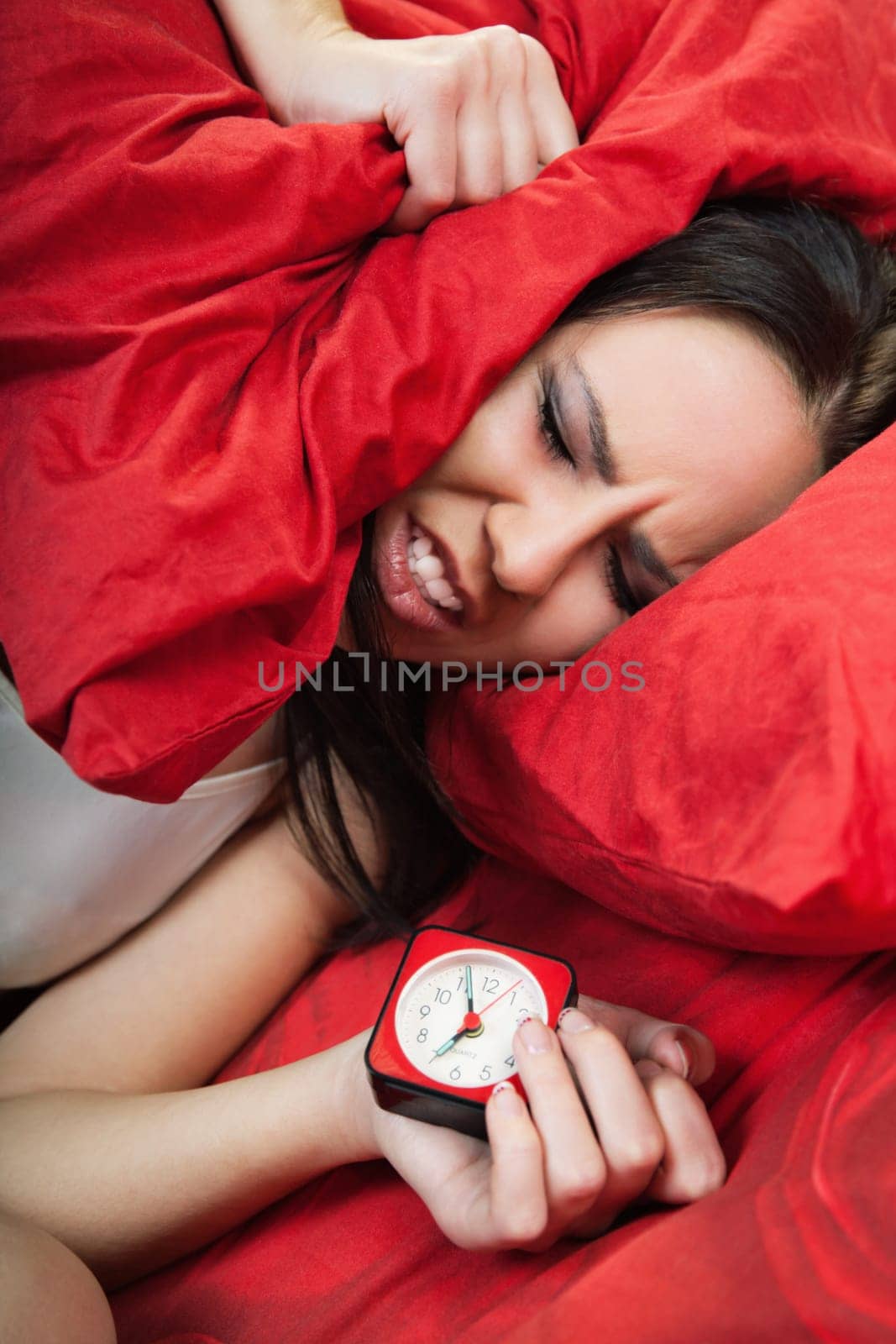 irritated young woman lying in bed and closing her ears with pillow