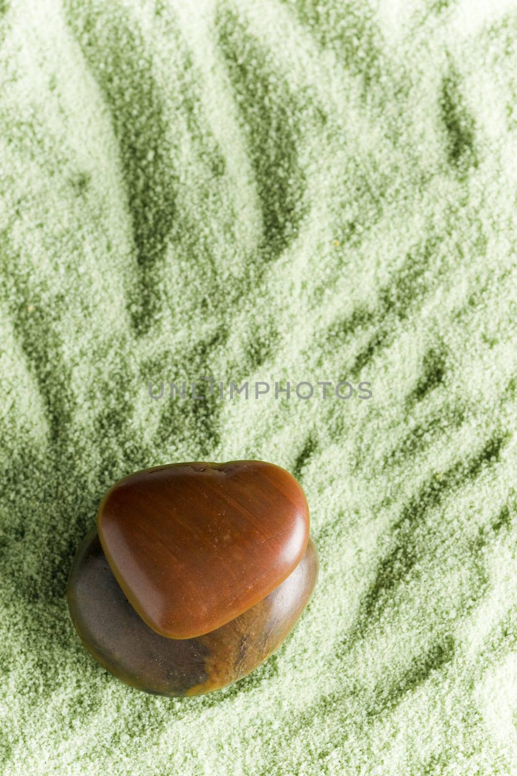 Brown stones in balance on green sand