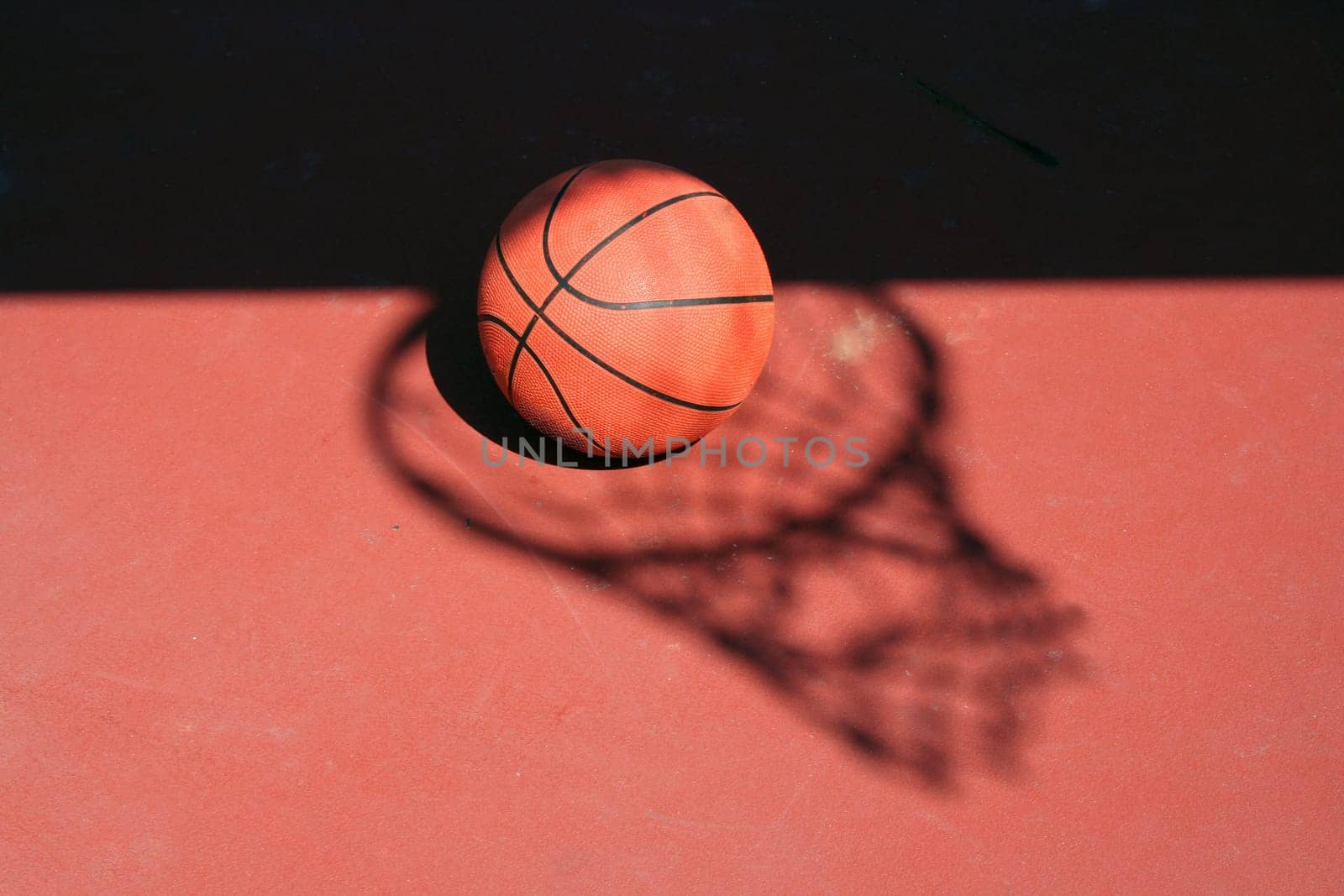 A Basketball and net shadow on a red court