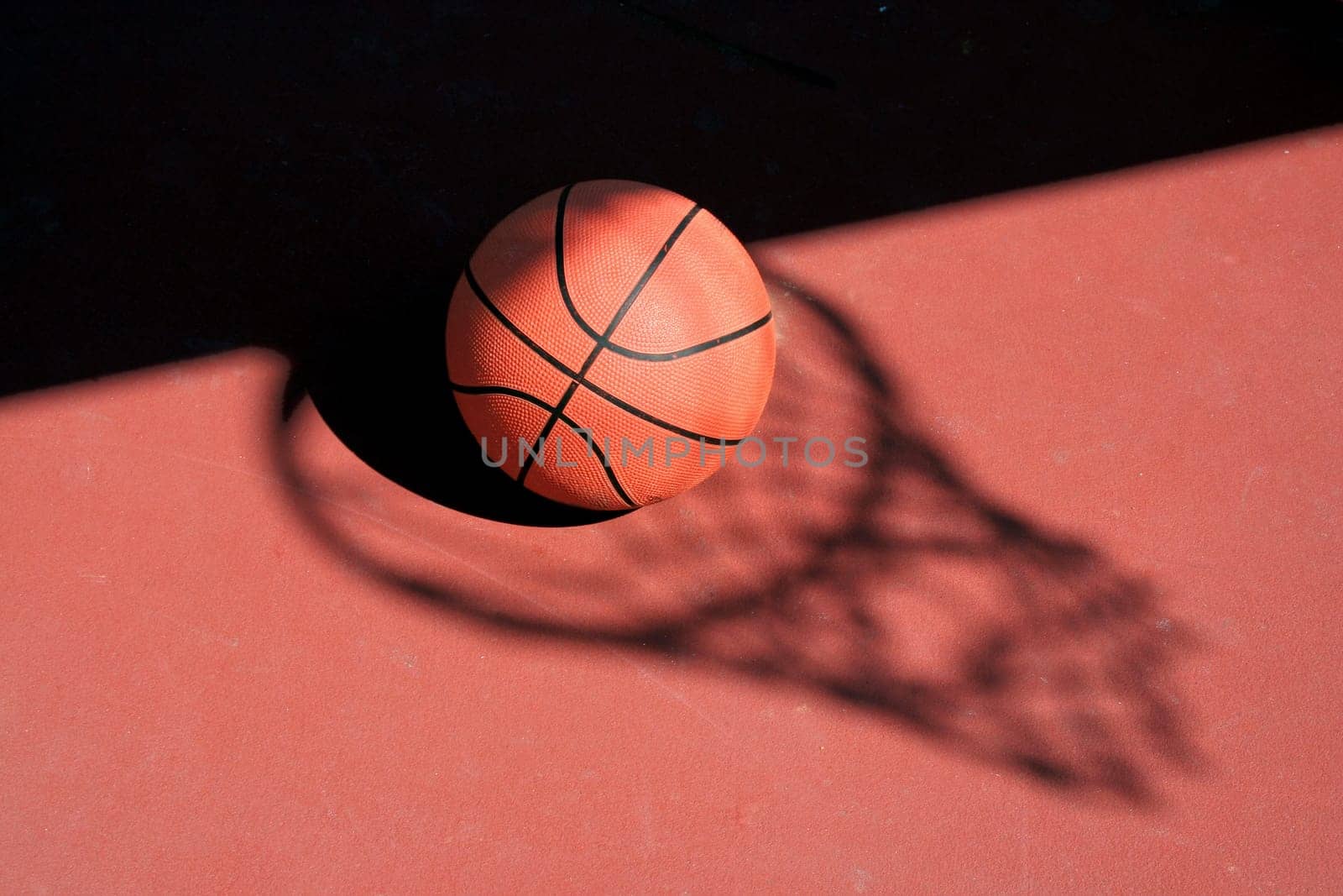 A Basketball and net shadow on a red court