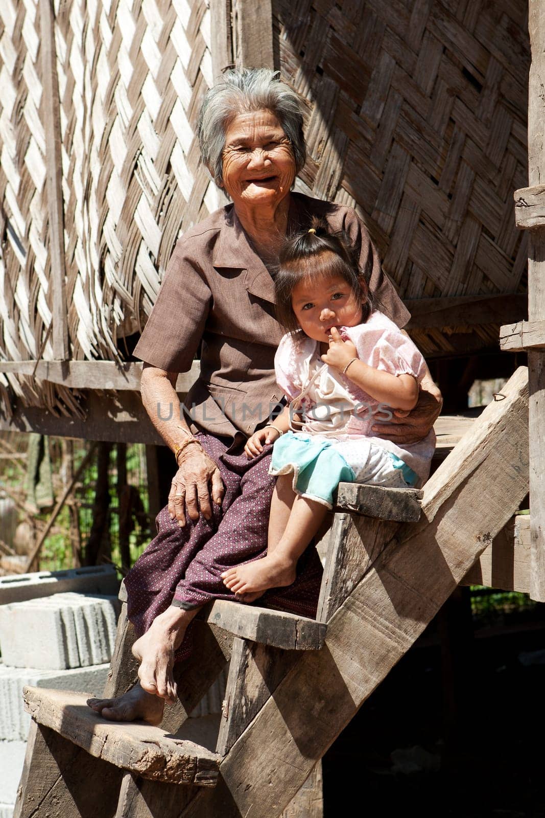 Asian grandmother with grandchild,portrait in front of Laotian house