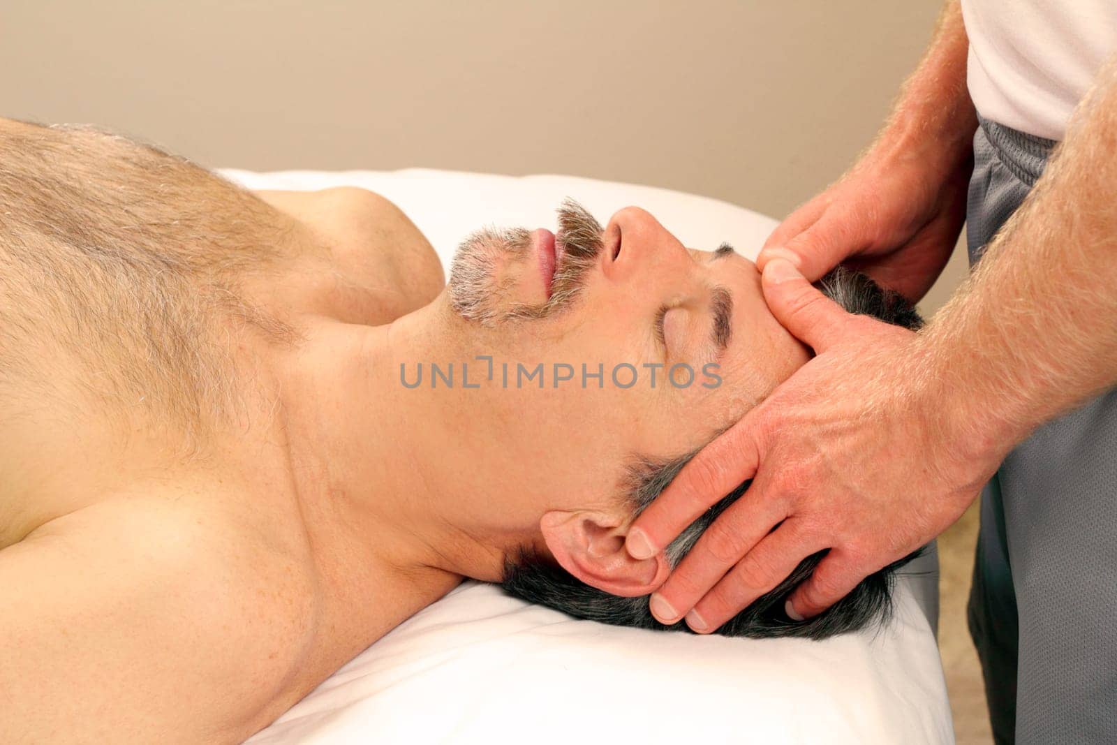 Mature guy receiving a relaxing facial massage from a masseur at a day spa.