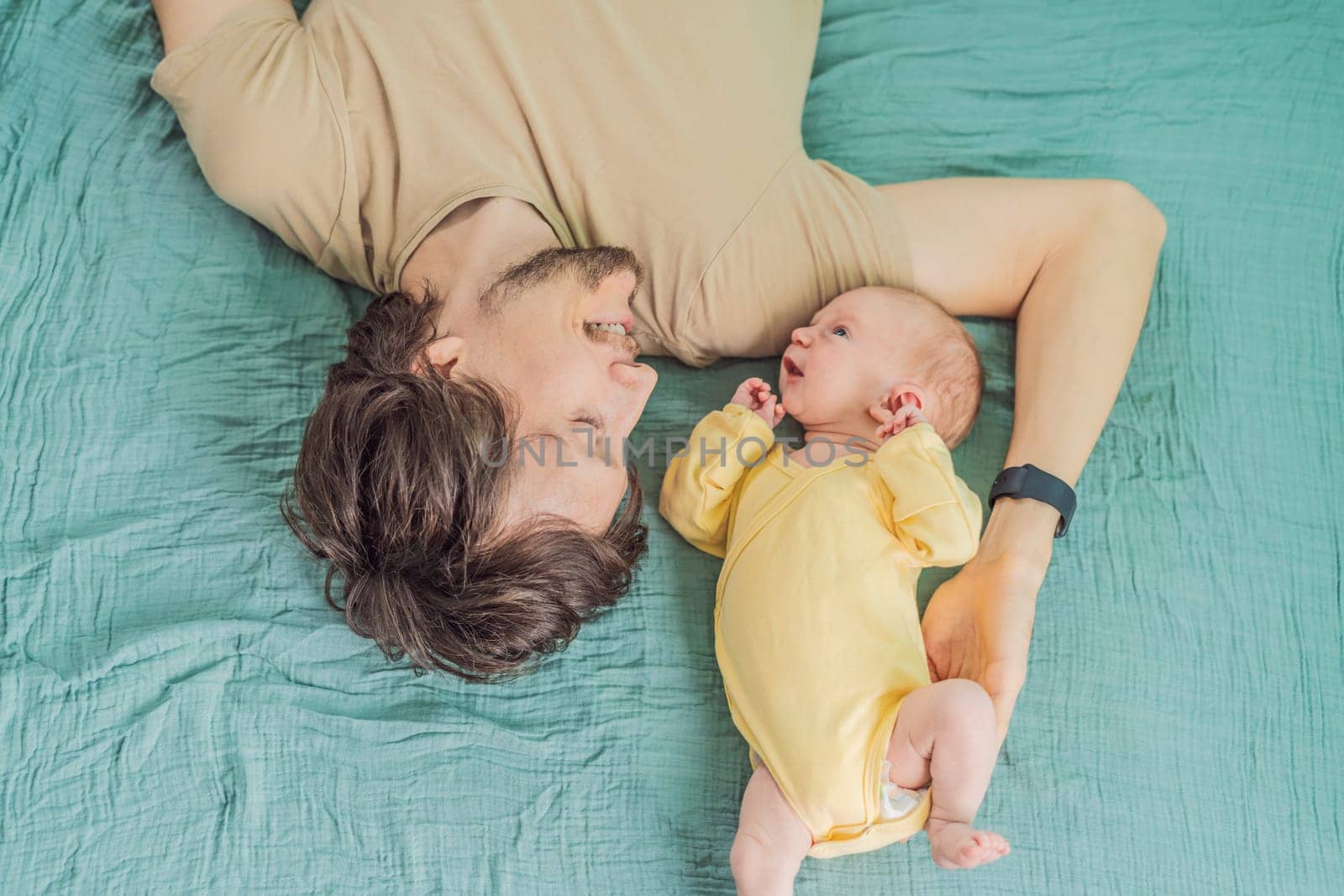 A father and his newborn baby lie on a soft muslin swaddle head to head, sharing a tender moment of closeness and bonding that highlights new beginnings and gentle parenting.