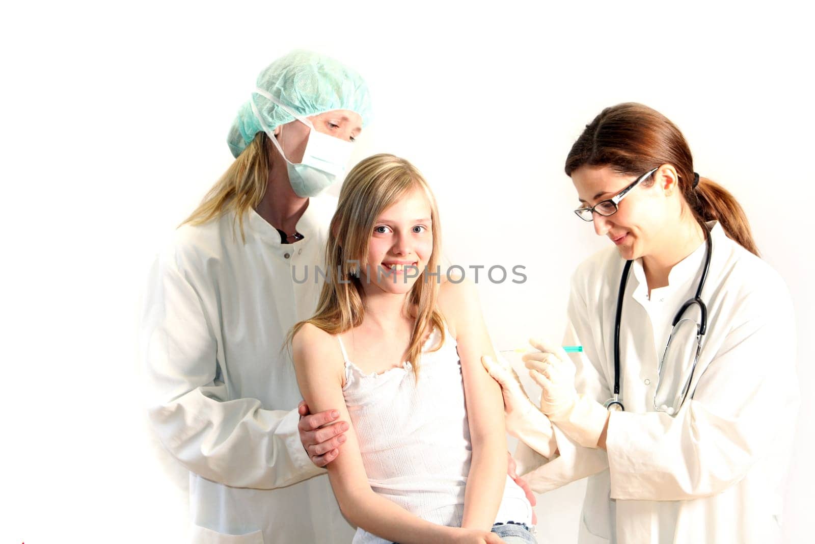Smiling child receives injection in upper arm from a female doctor. A nurse or doctor lovingly holds the child.