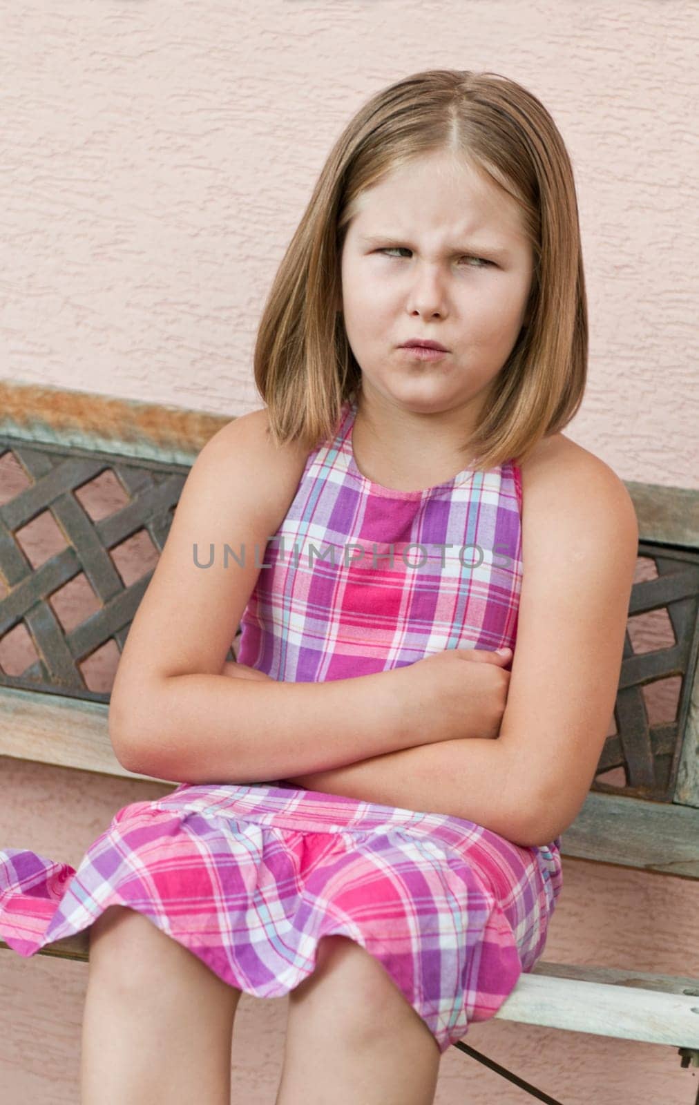 Outdoors portrait of small cute girl sitting on bench with angry expression