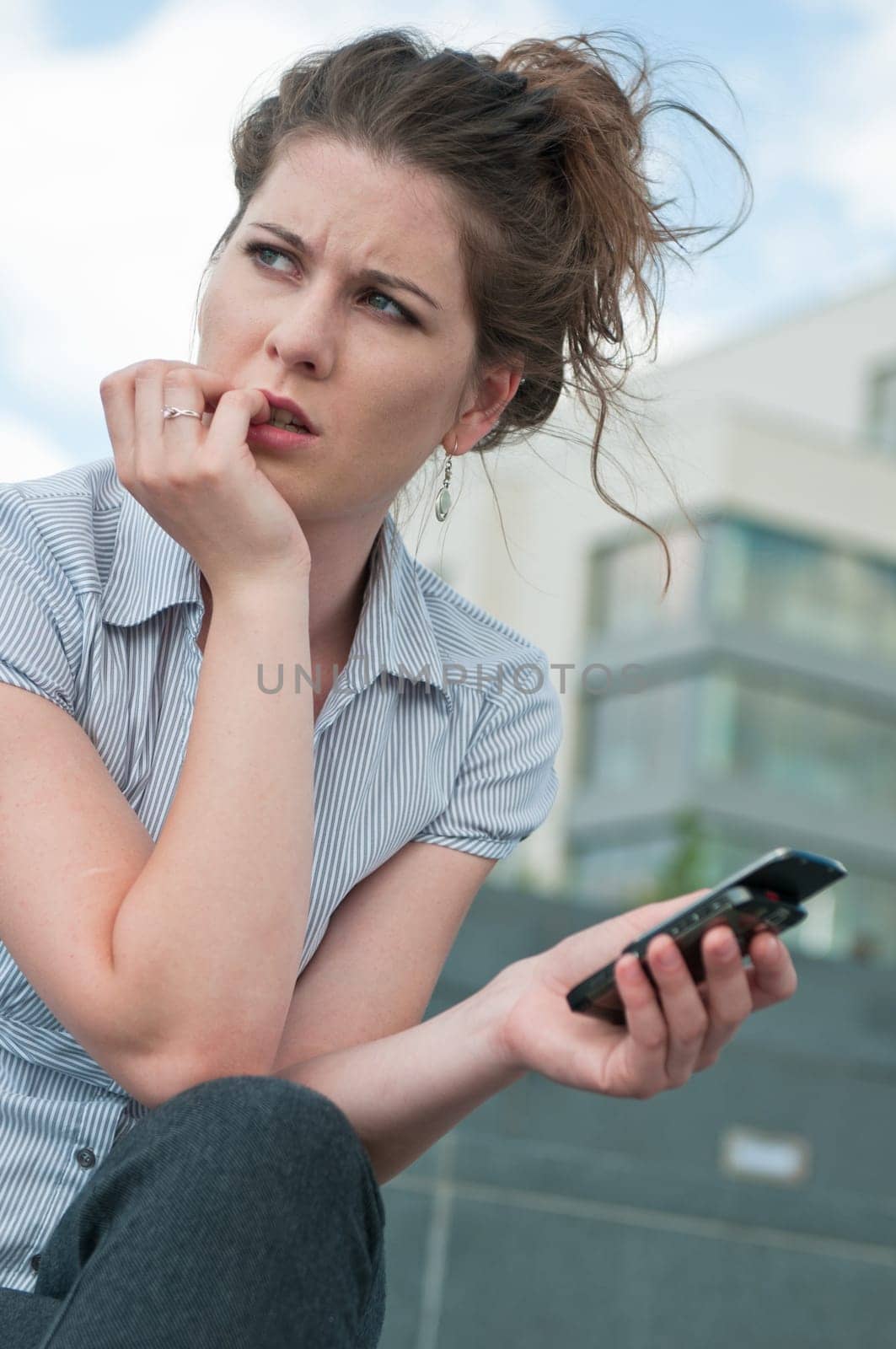 Young worried woman with unhappy expression holding mobile phone - outdoors in urban setting