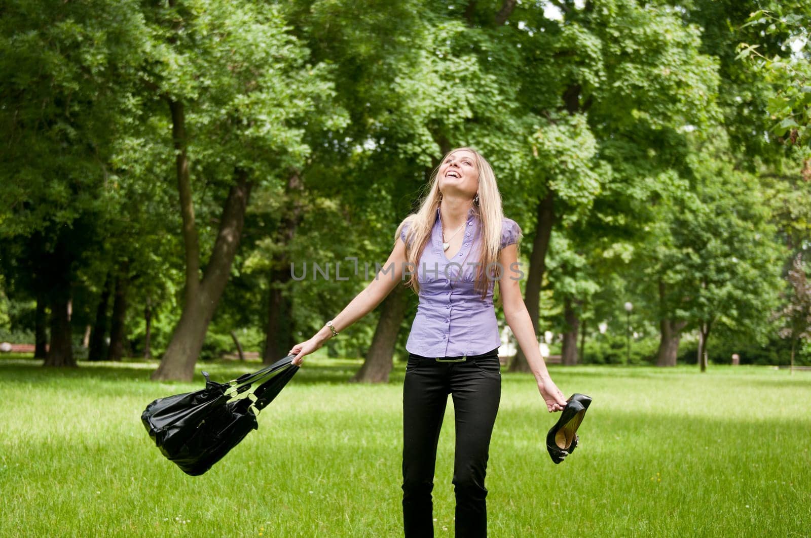 Young woman enjoying life outdoors - spinning around and holding bag and shoes