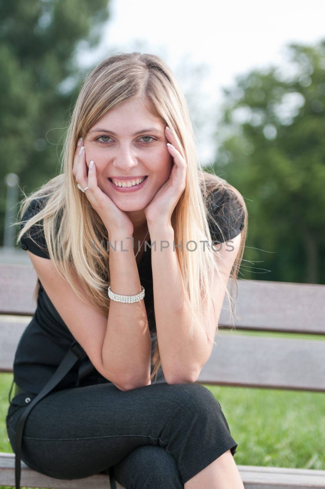 Portrait of young beautiful smiling woman siting on bench in park outside