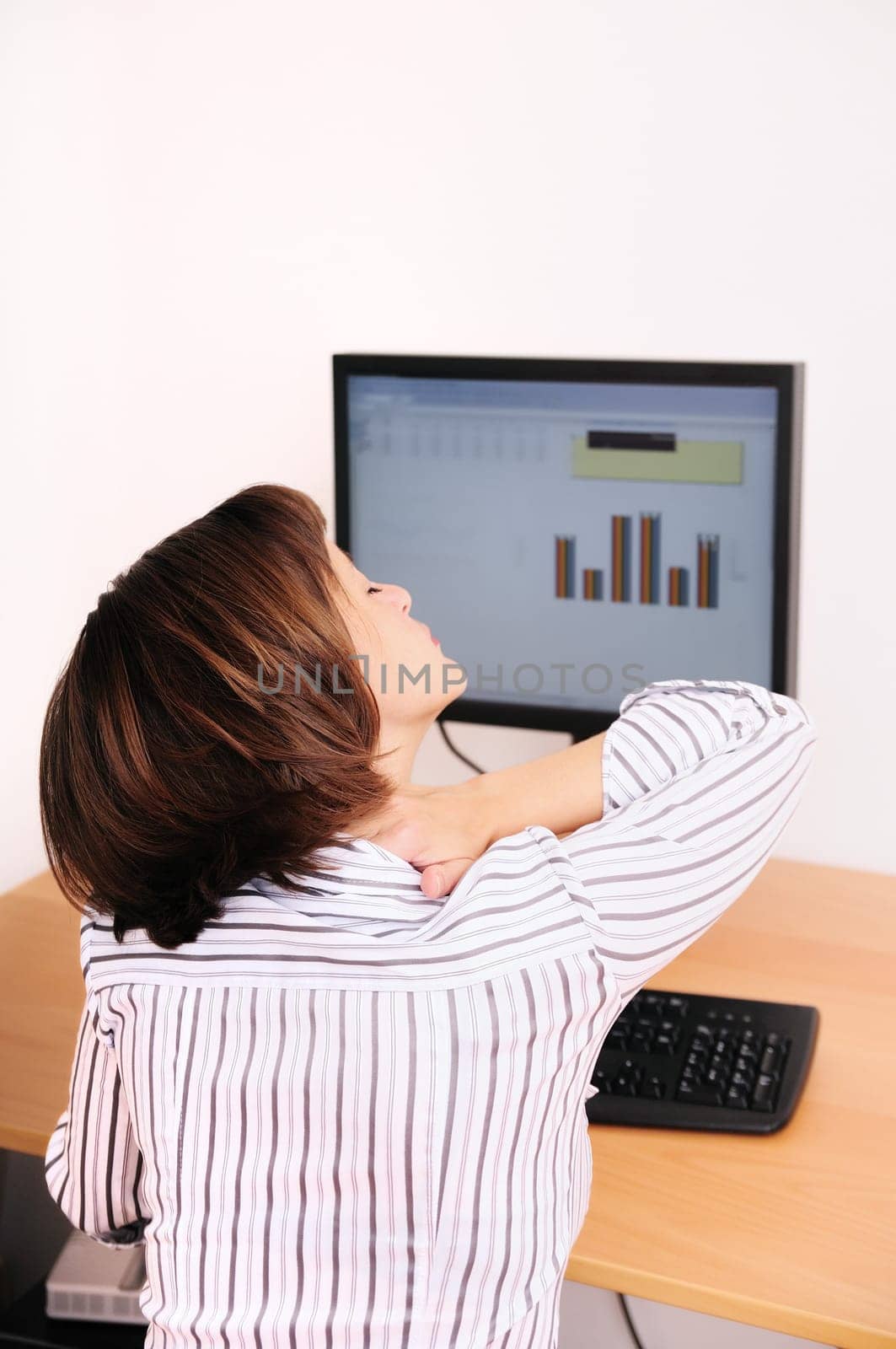 Business woman with neck pain. Focus on hand on neck with blurred monitor on table in background.
